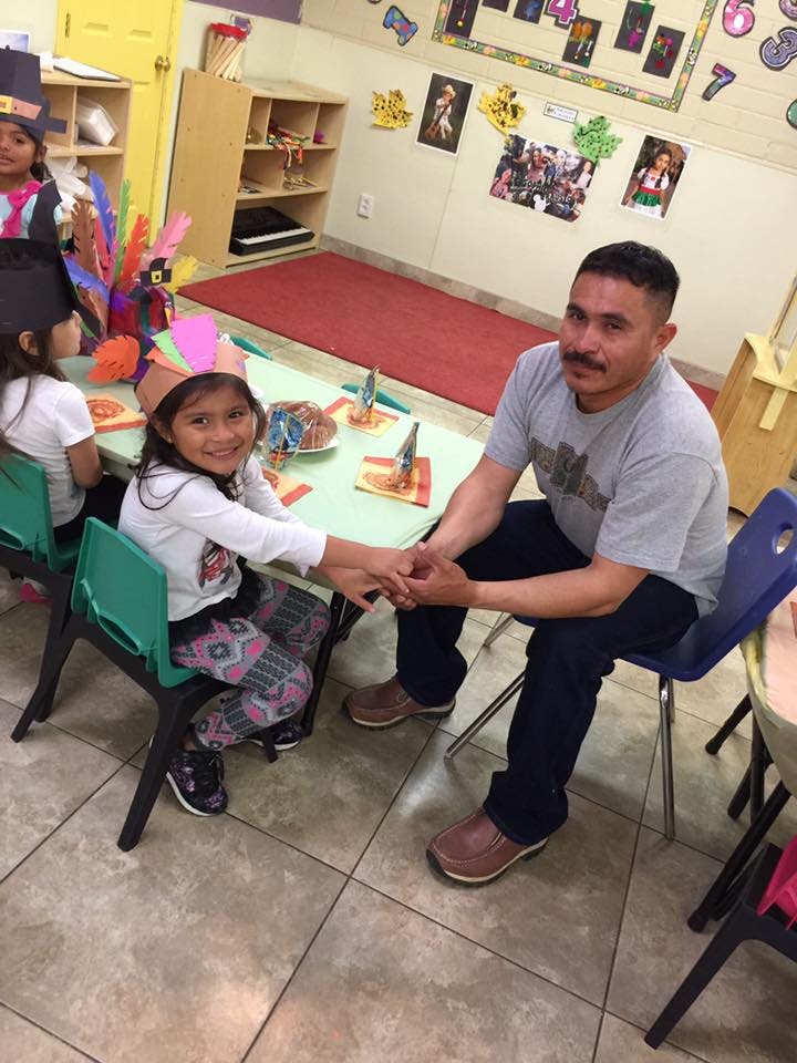 Adult and child holding hands at a table in a classroom