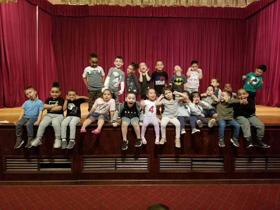 Group of children sitting on a stage with red curtains