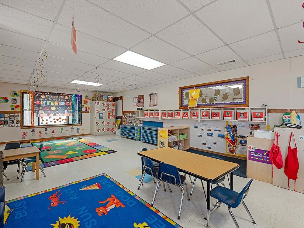 A colorful classroom with child-sized tables and chairs, bright rugs, and decorated walls