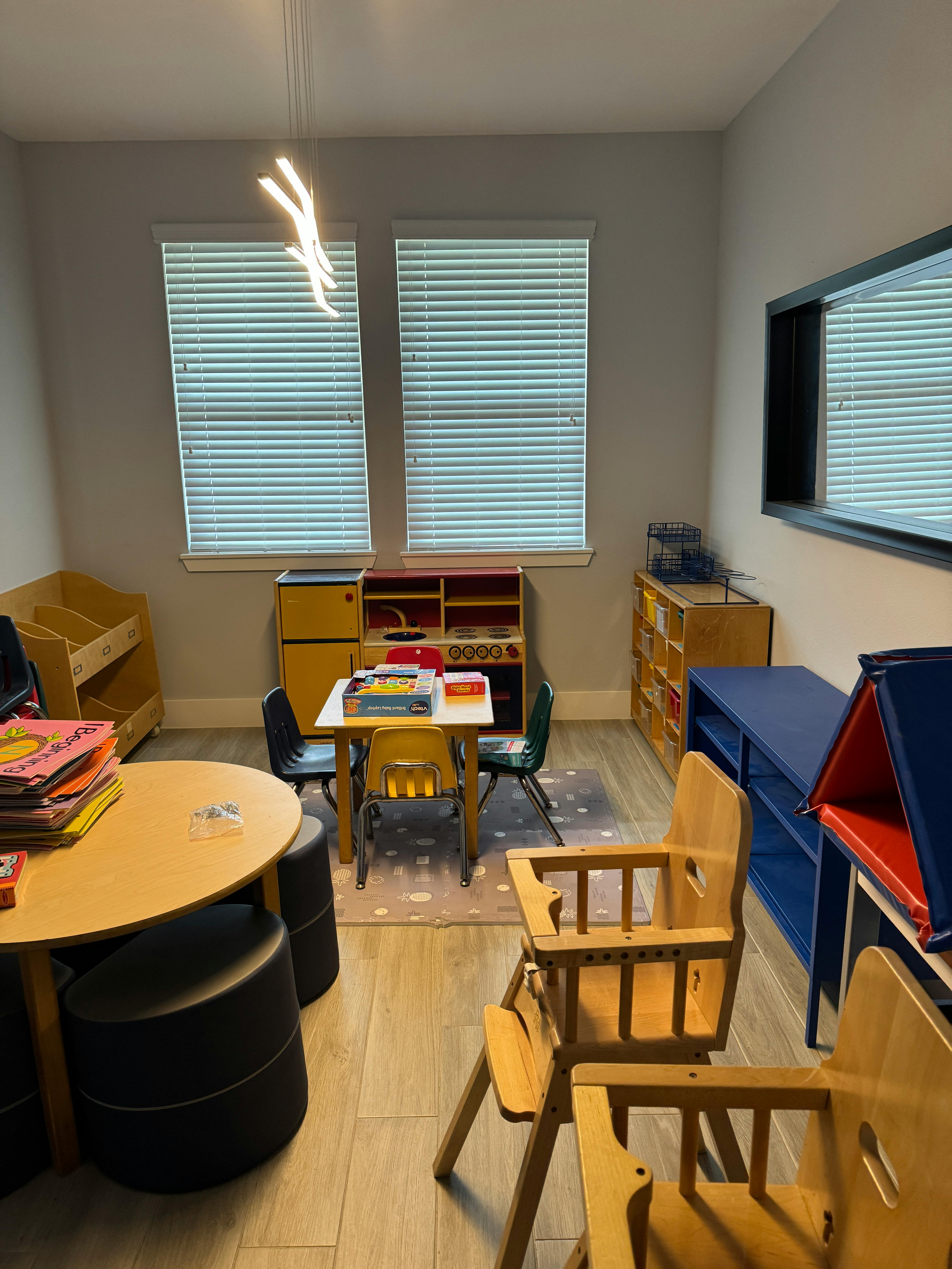 Classroom with small tables and chairs, shelves, and windows with blinds on windows