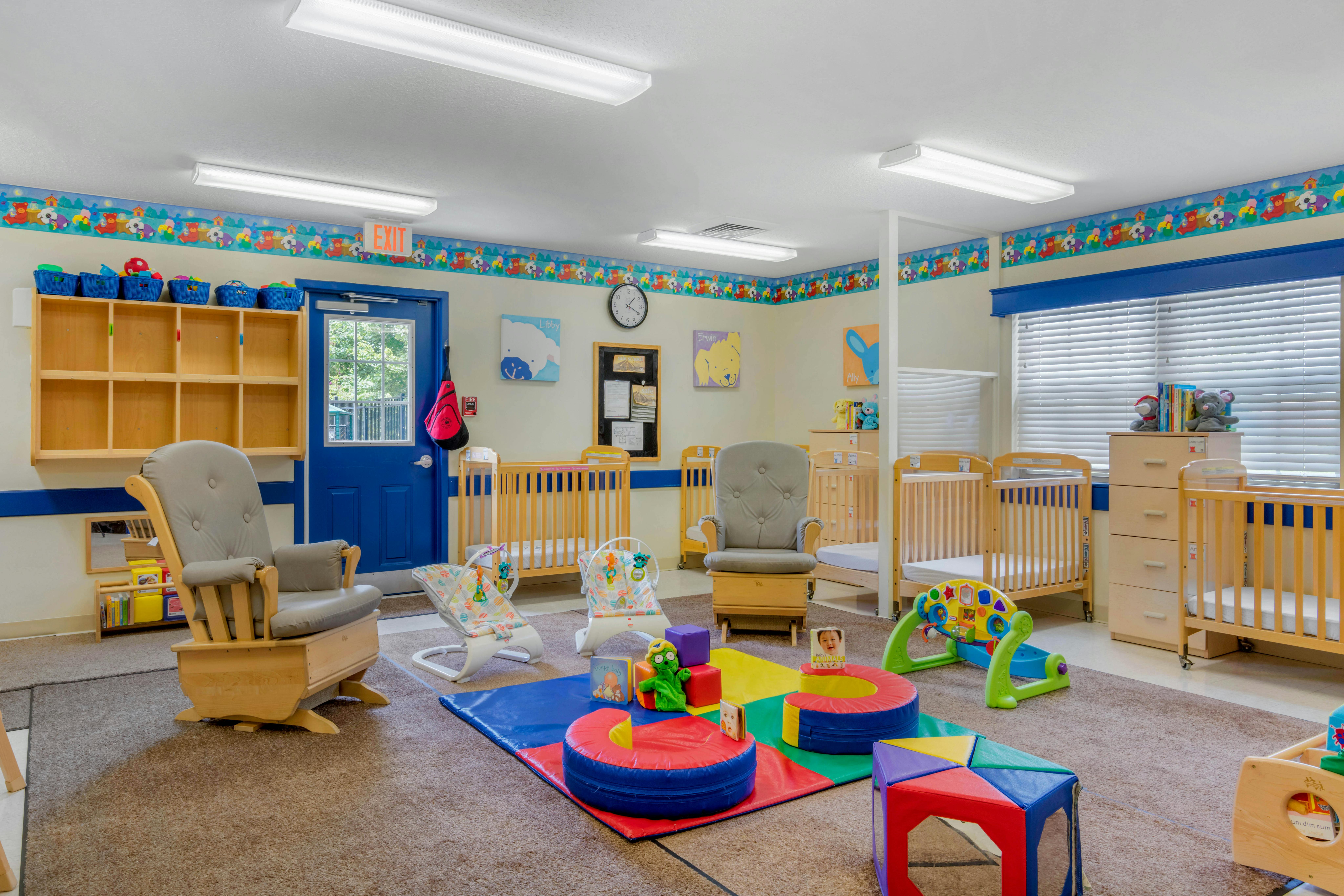 A colorful nursery room with multiple cribs, two rocking chairs, and infant playmats