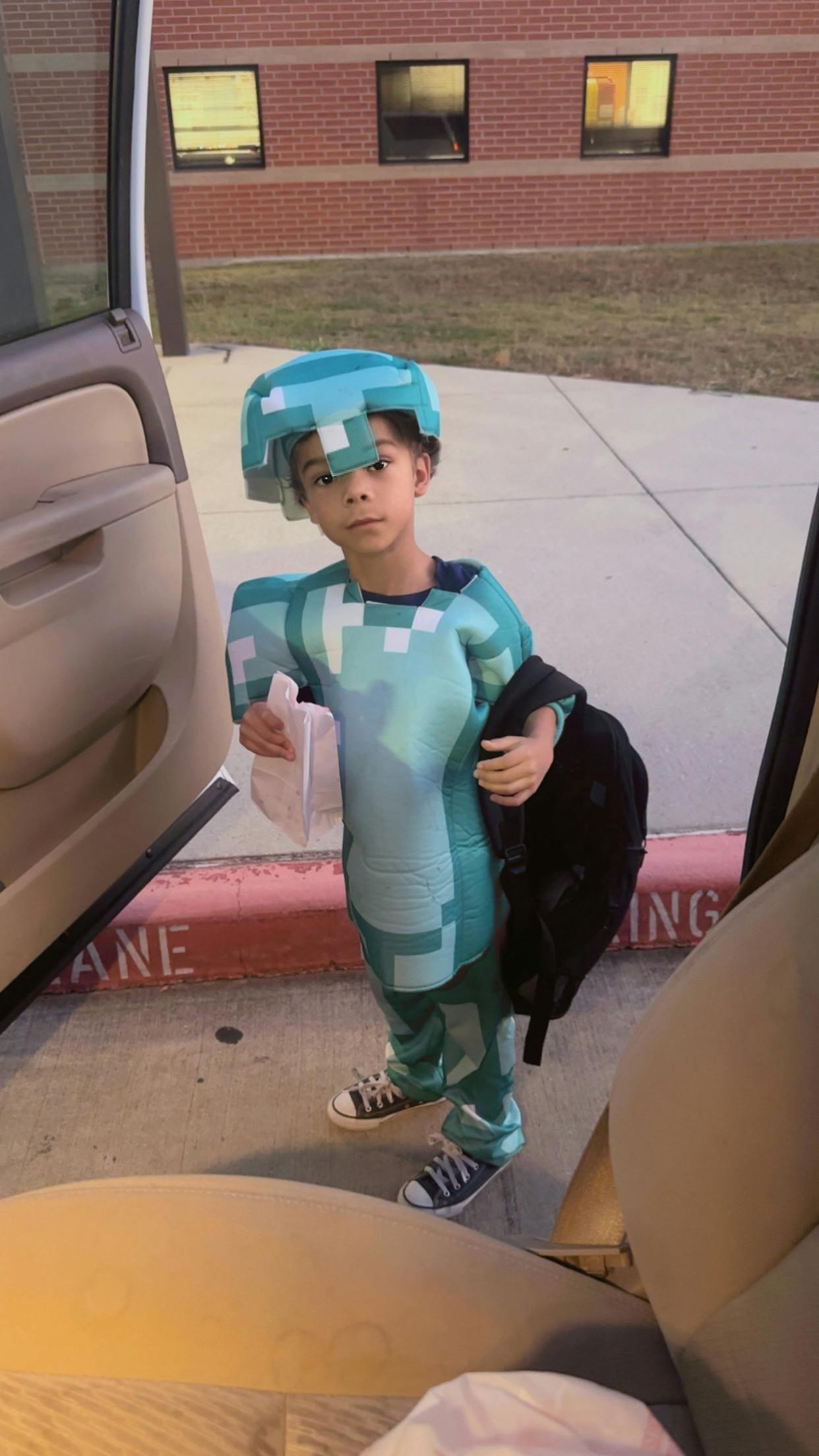 Child in a pixelated costume standing by an open car door