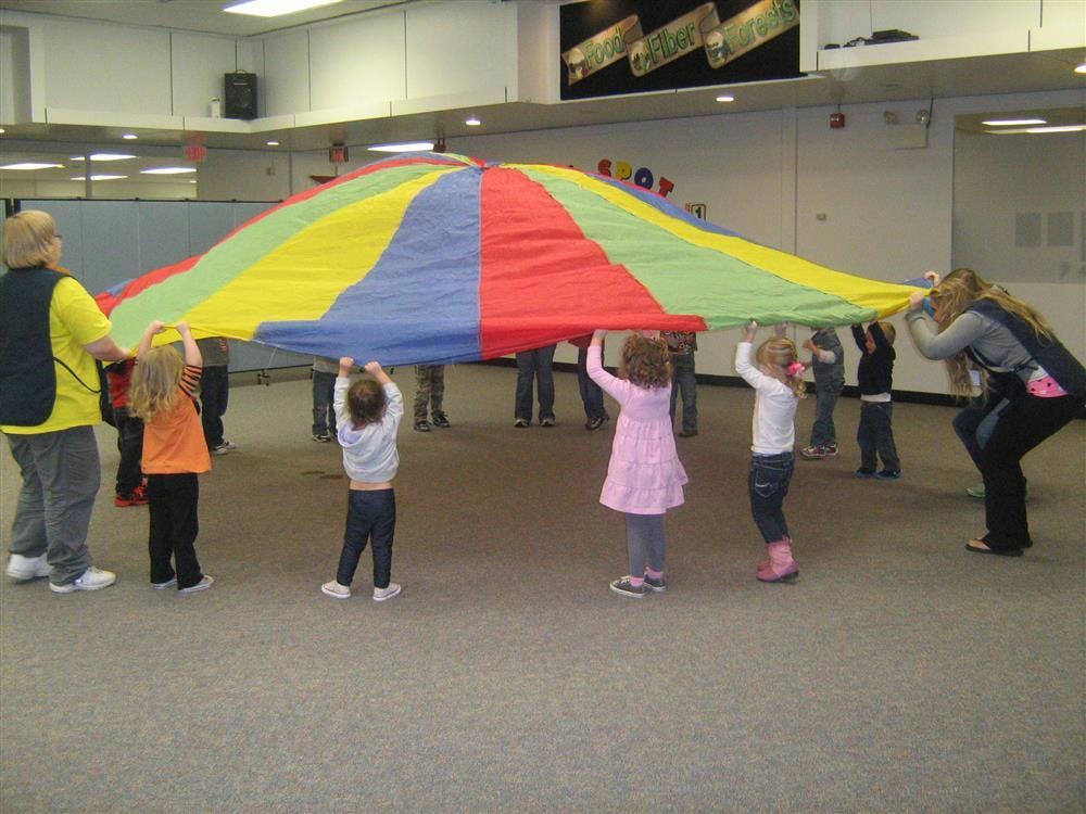 People and children holding up a colorful parachute indoors