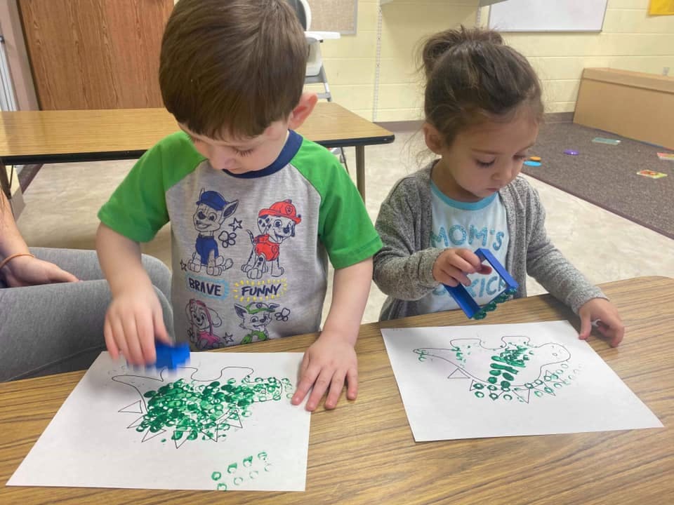Two children stamping green paint onto paper in a classroom