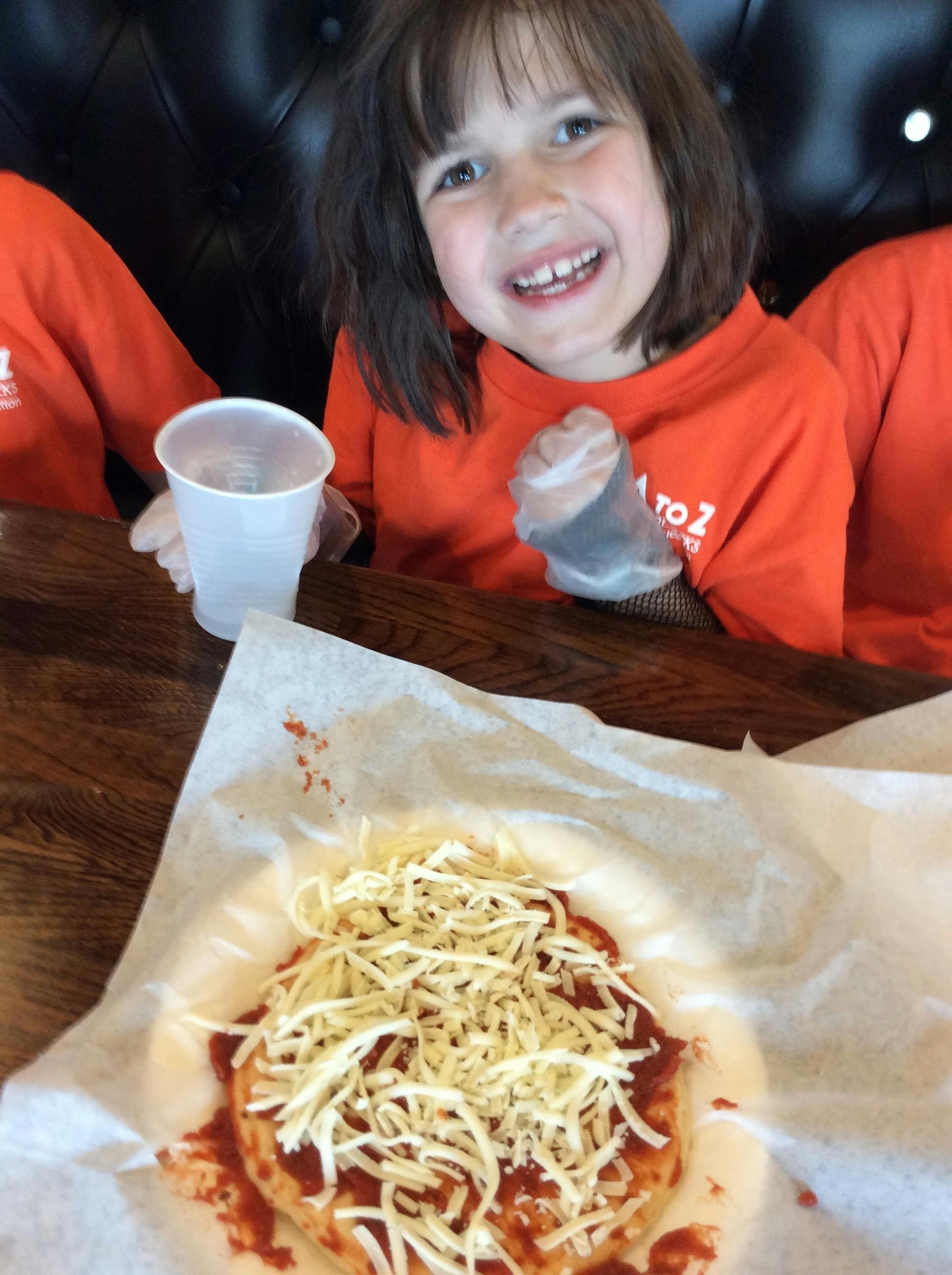 Child wearing plastic gloves preparing a pizza on wax paper