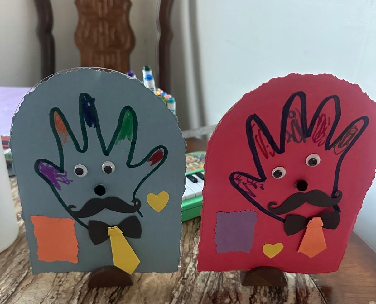 Two paper handprint crafts decorated with googly eyes and bow ties