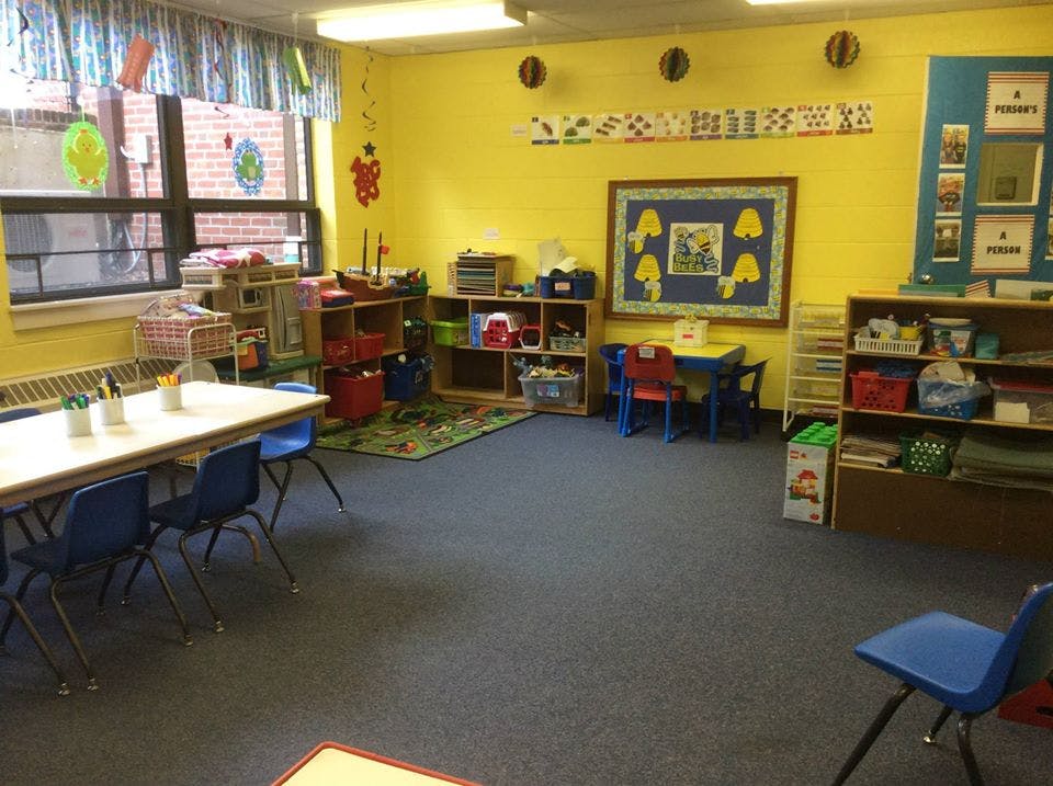 Empty classroom with yellow walls, tables, chairs, and shelves
