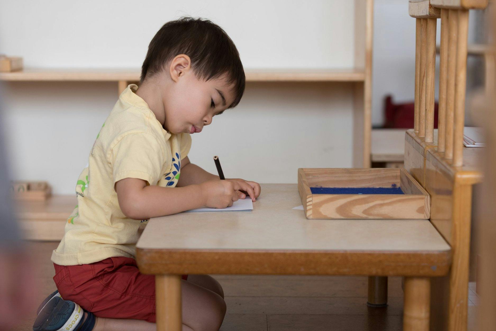 Child writing on paper at a small table
