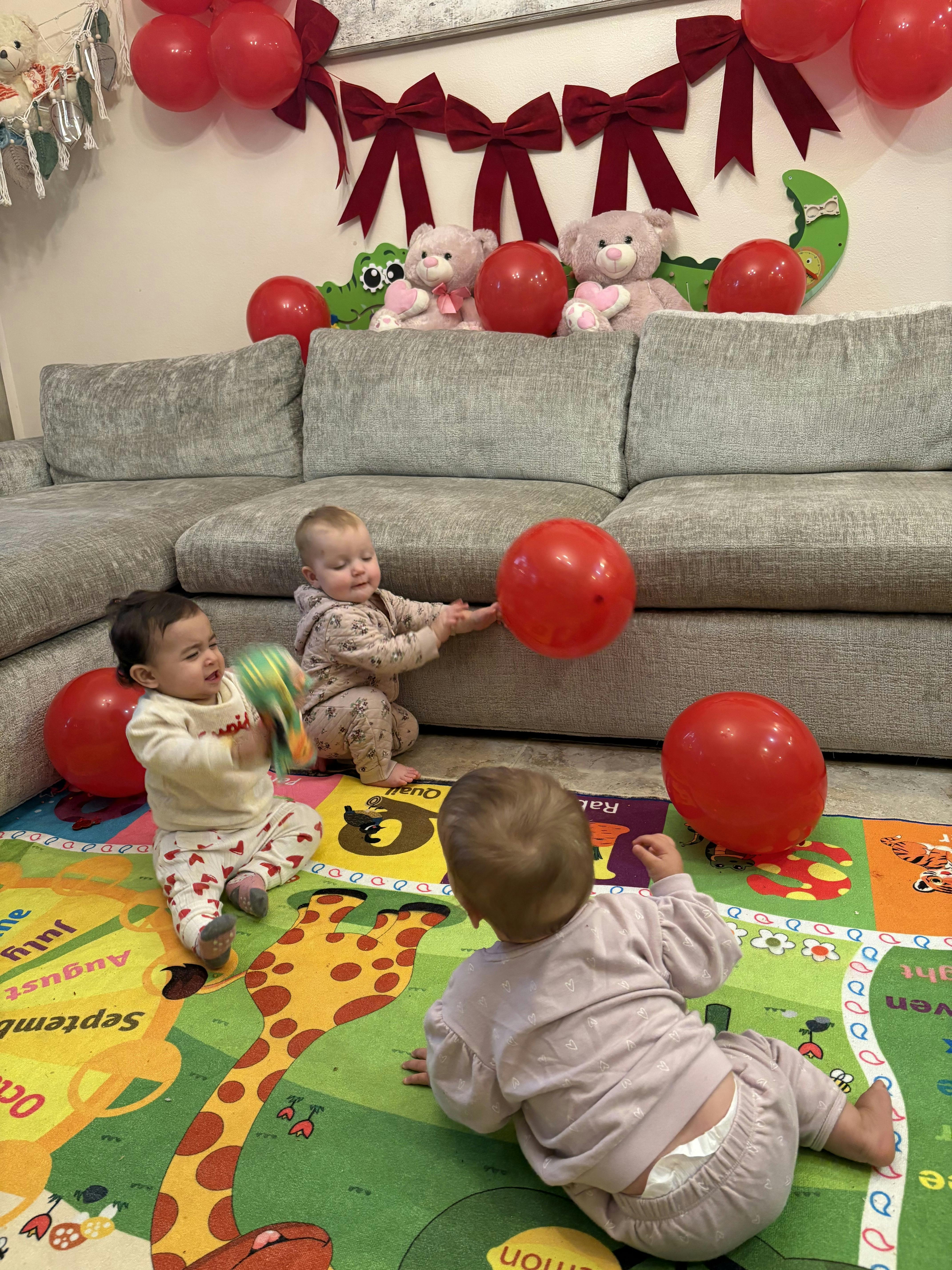Three children playing on a colorful mat with red balloons