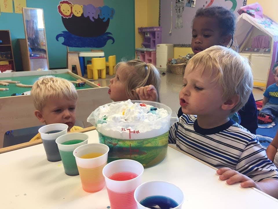 Children looking at a container of white foam and cups of colored liquid