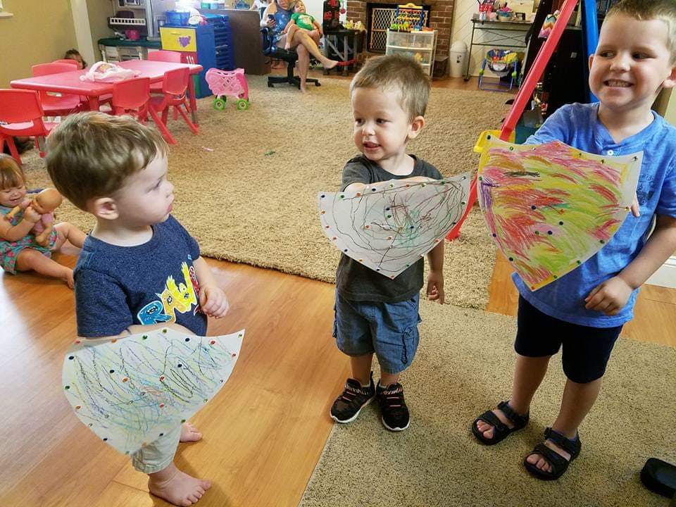 Three children holding up their artwork in a classroom
