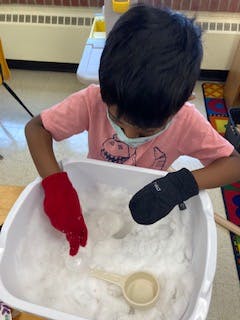Child wearing mittens playing with ice in a bin