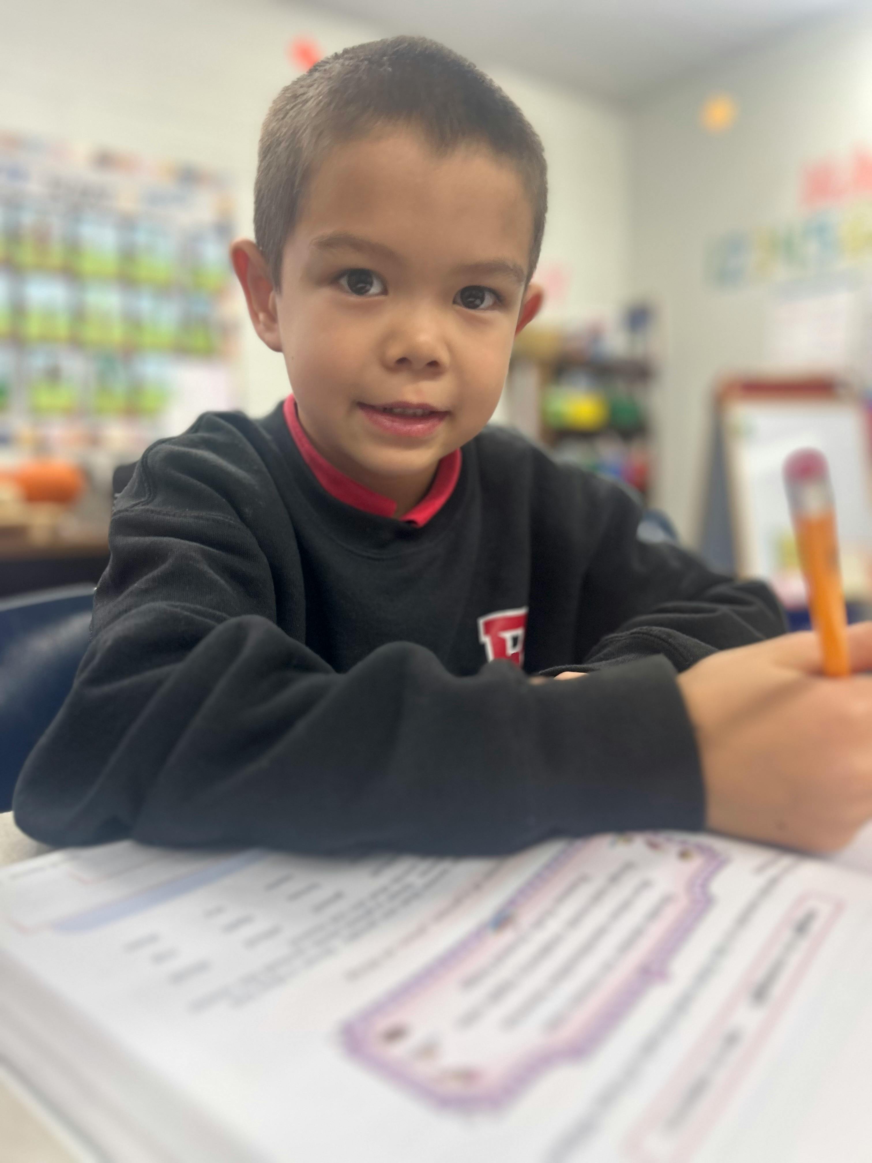 Child in a classroom writing on paper with a pencil