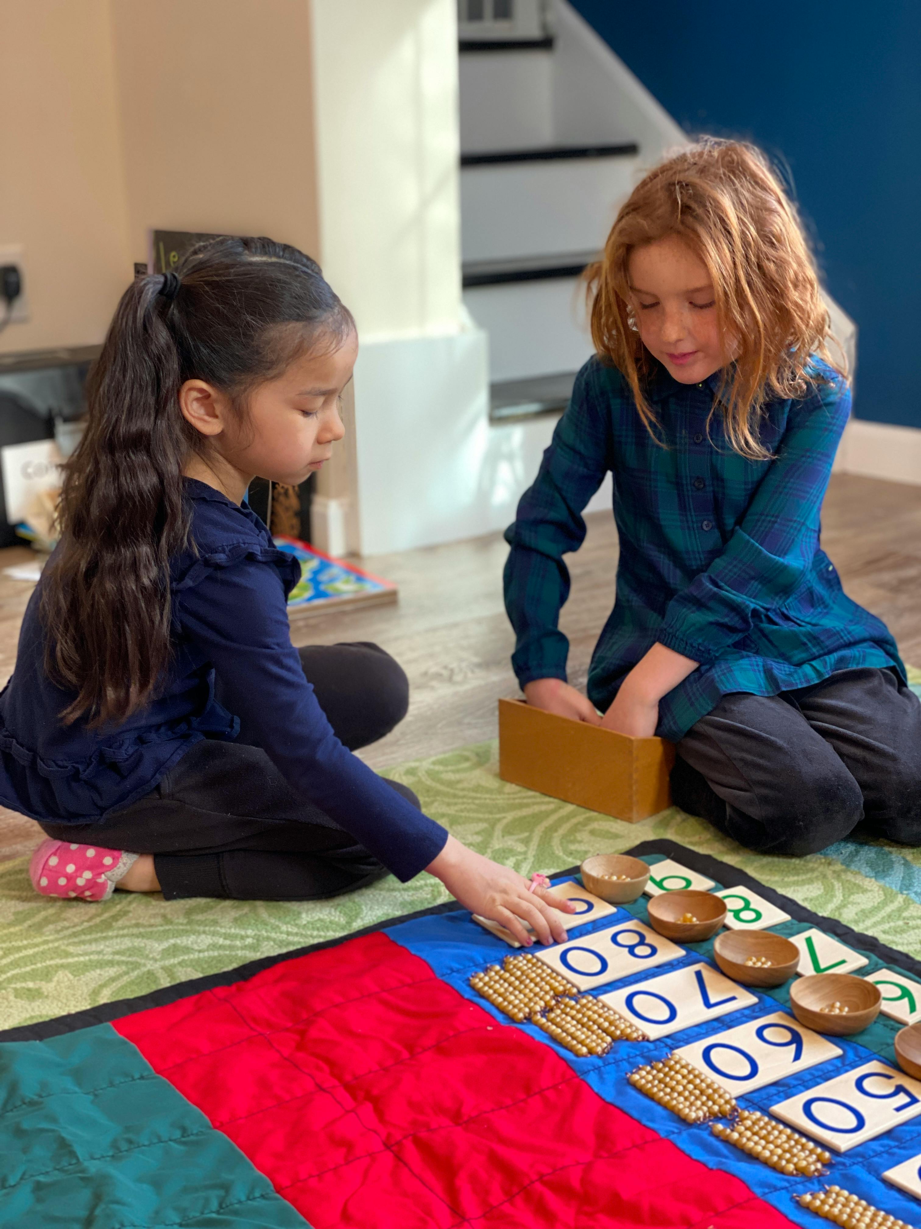 Two children playing with counting beads and number cards on a mat