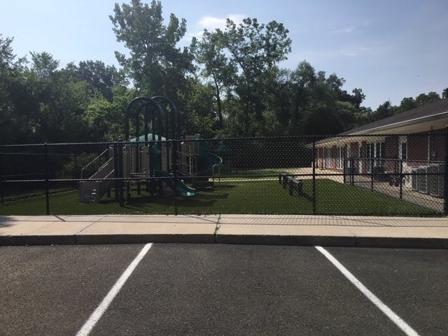 Empty playground with artificial turf next to a brick building and parking lot