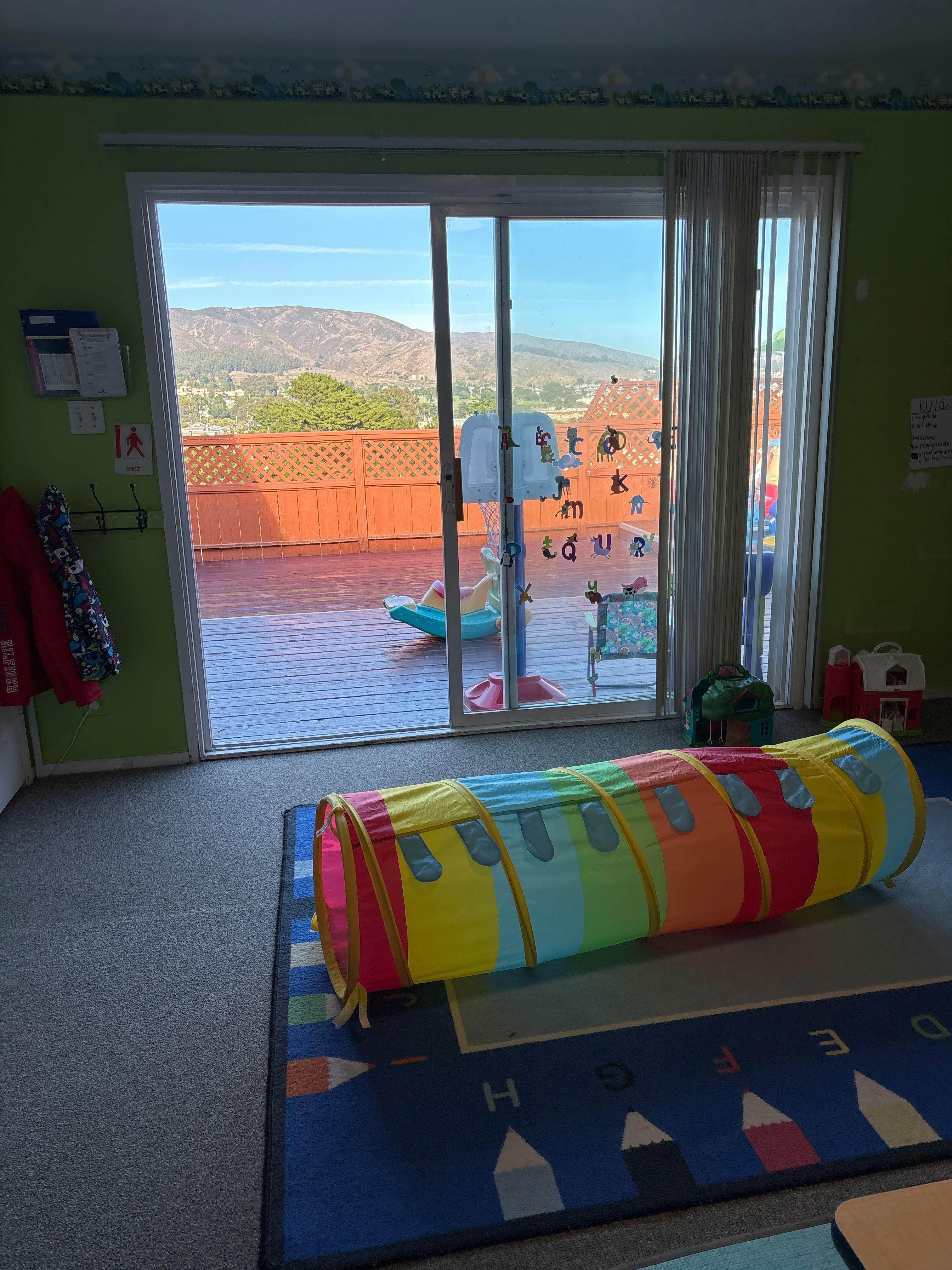 Play tunnel on a rug in a room with a sliding glass door to a deck