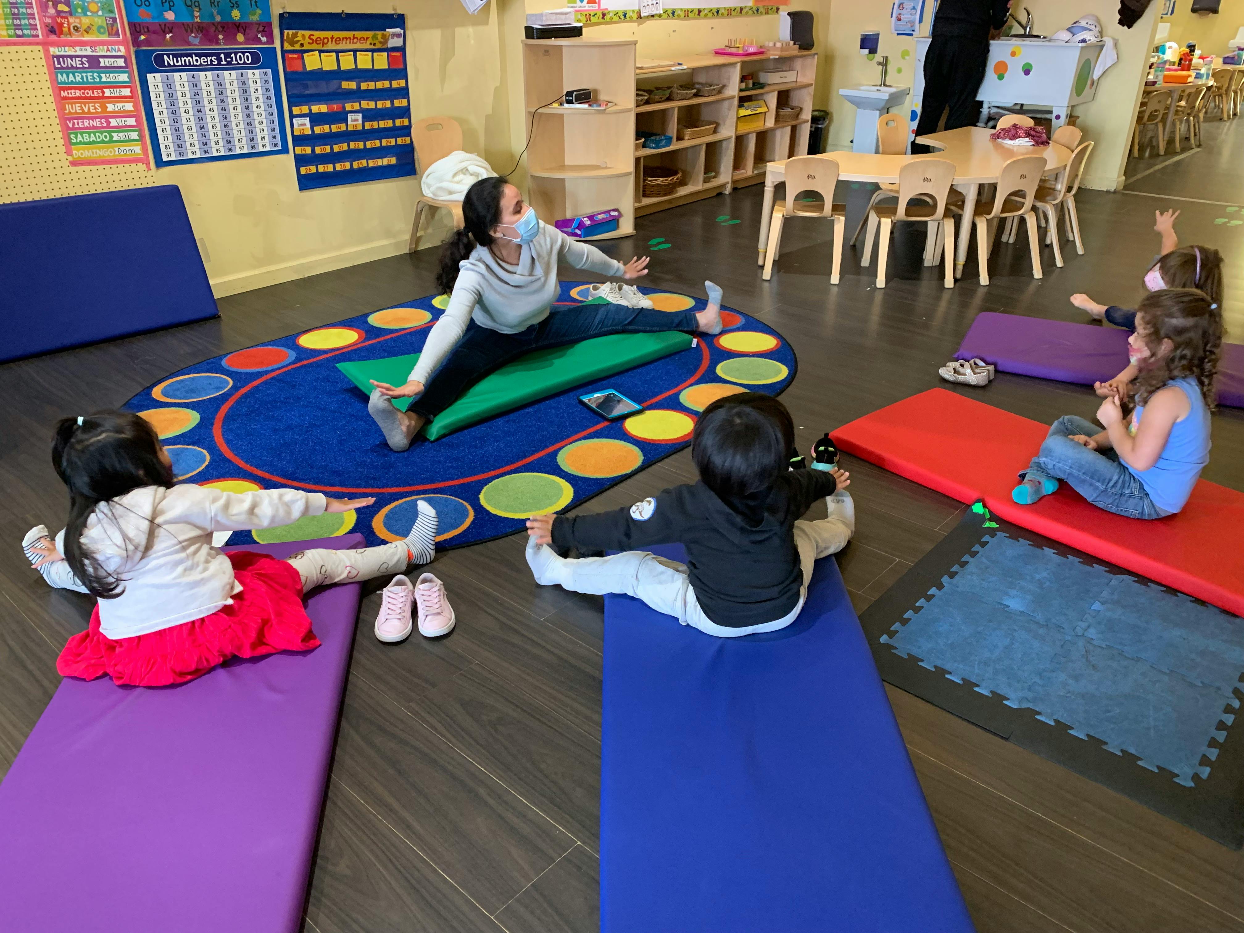 Adult and children doing yoga poses on mats in a classroom
