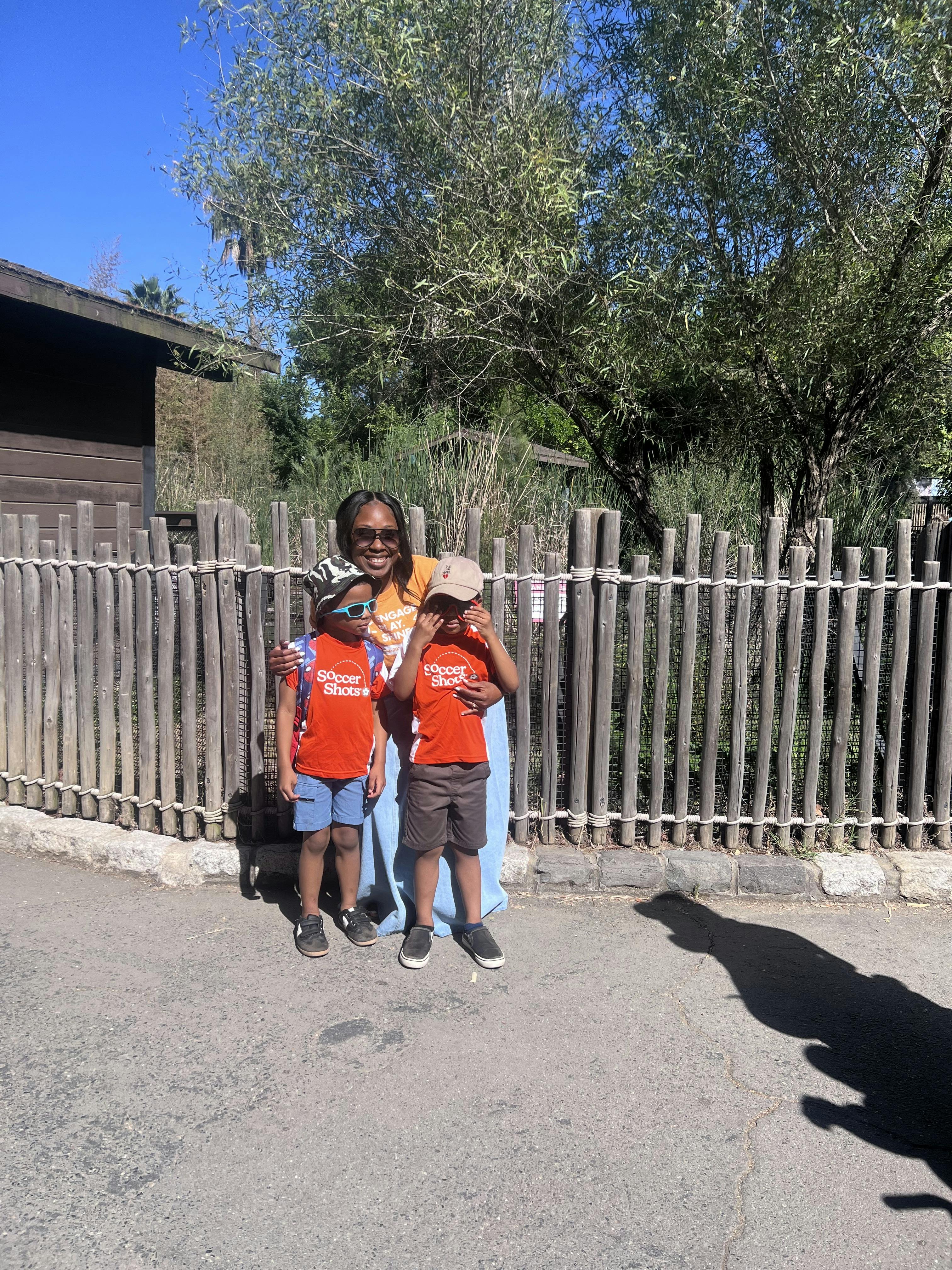 Adult standing with two children wearing matching orange Soccer Shots shirts