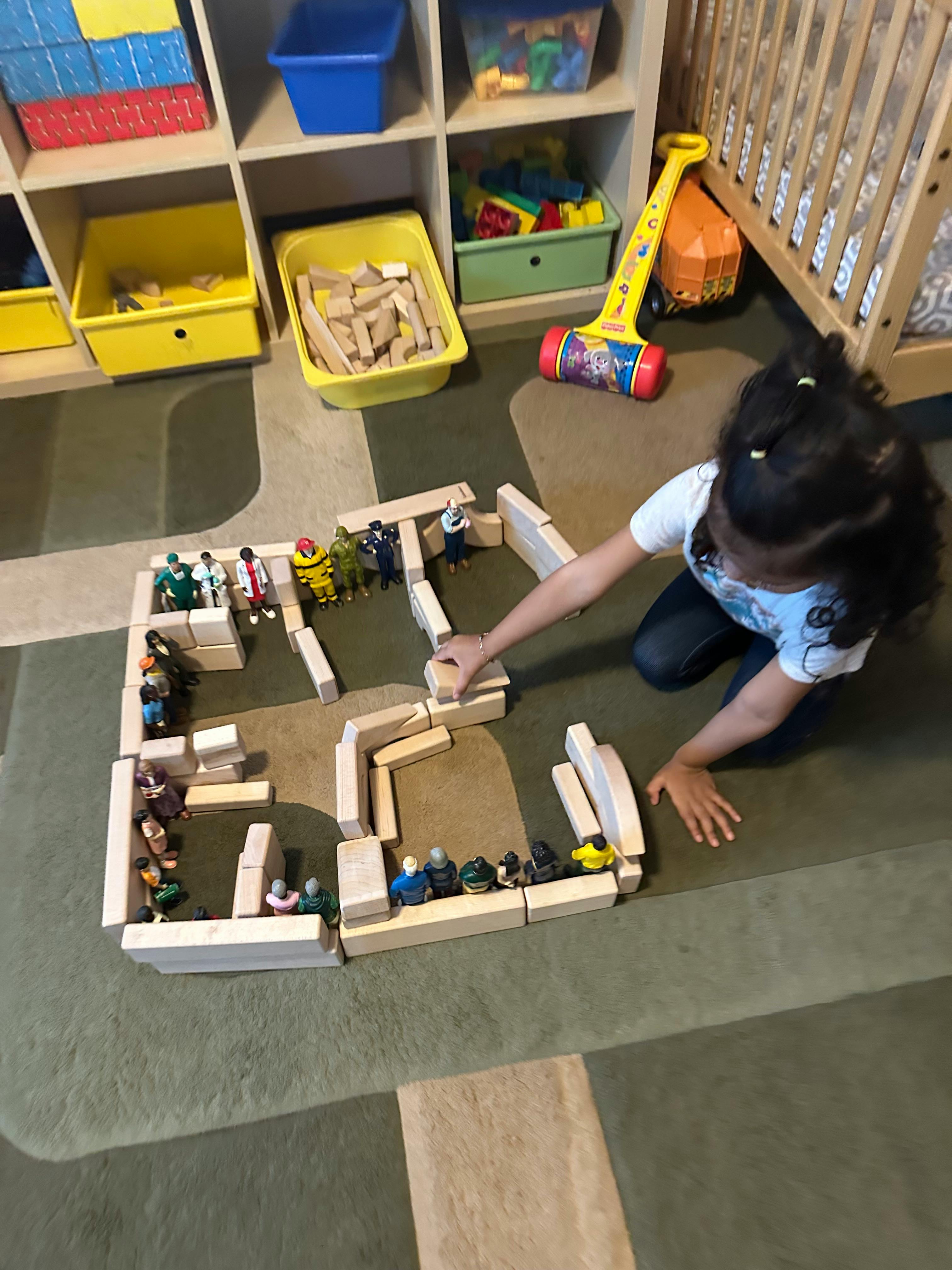 Child playing with wooden blocks and small figures on a rug