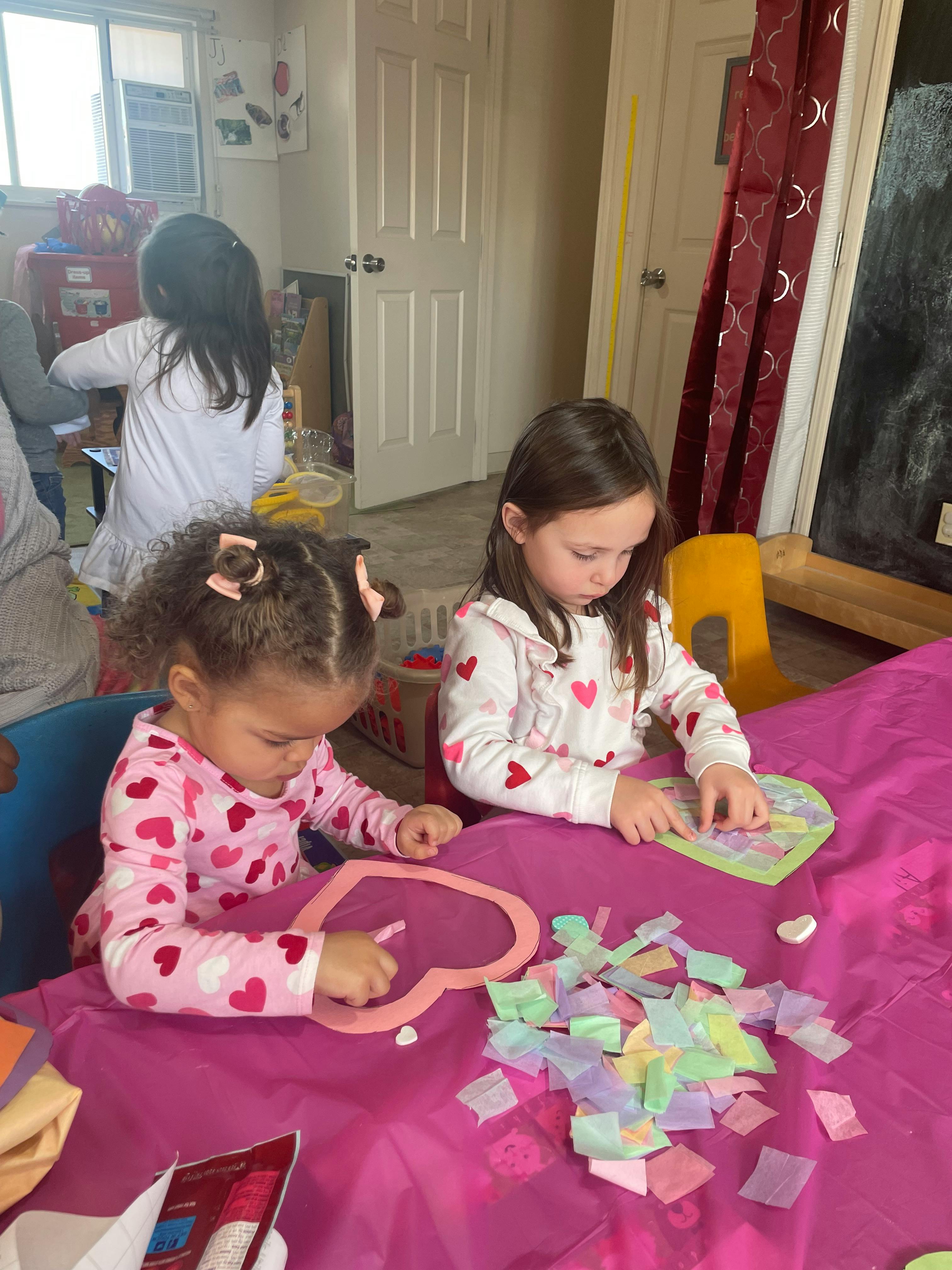 Two children making heart-shaped crafts with colorful paper pieces