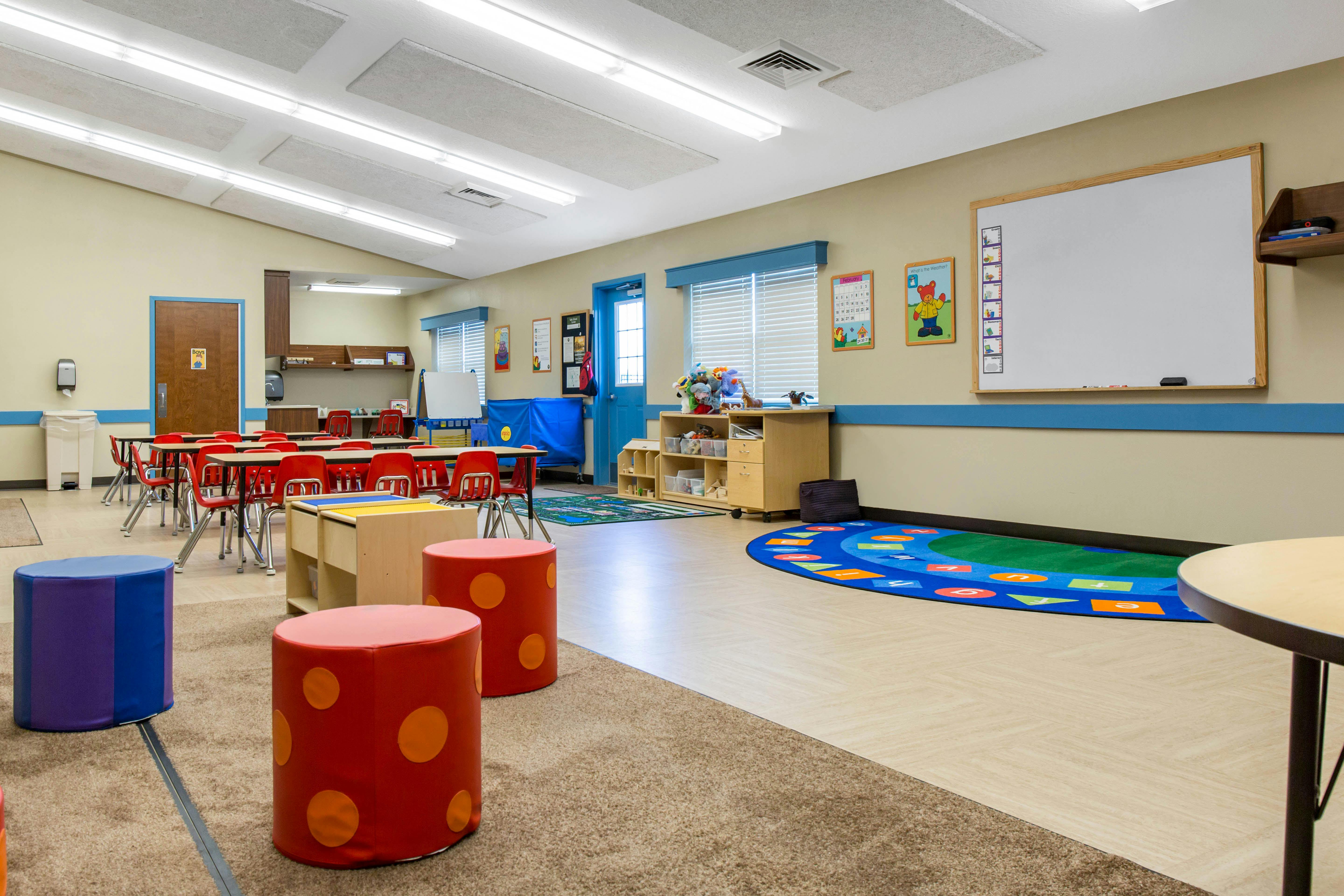 Classroom with small red chairs, tables, colorful rug, and whiteboards