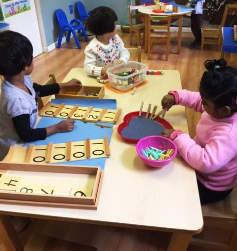 Three children playing with educational toys at a table in a classroom