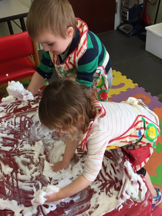 Two children playing with shaving cream on a red surface