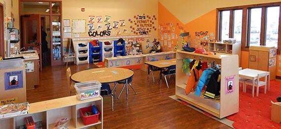 Empty classroom with small tables, chairs, and shelves with learning materials