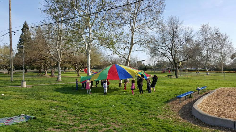 Children playing with a colorful parachute in a grassy park