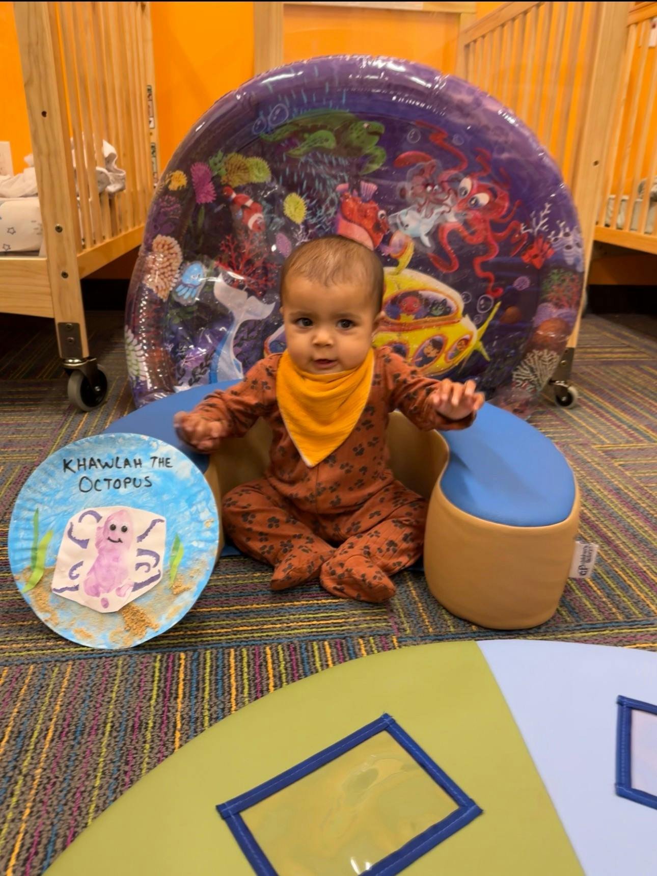 Child sitting on the floor with a paper plate craft and an inflatable toy