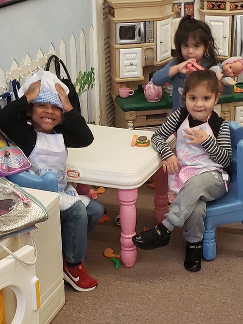 Three children playing in a pretend kitchen area