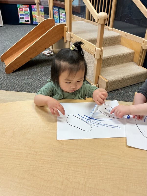 Child drawing on paper with a blue marker