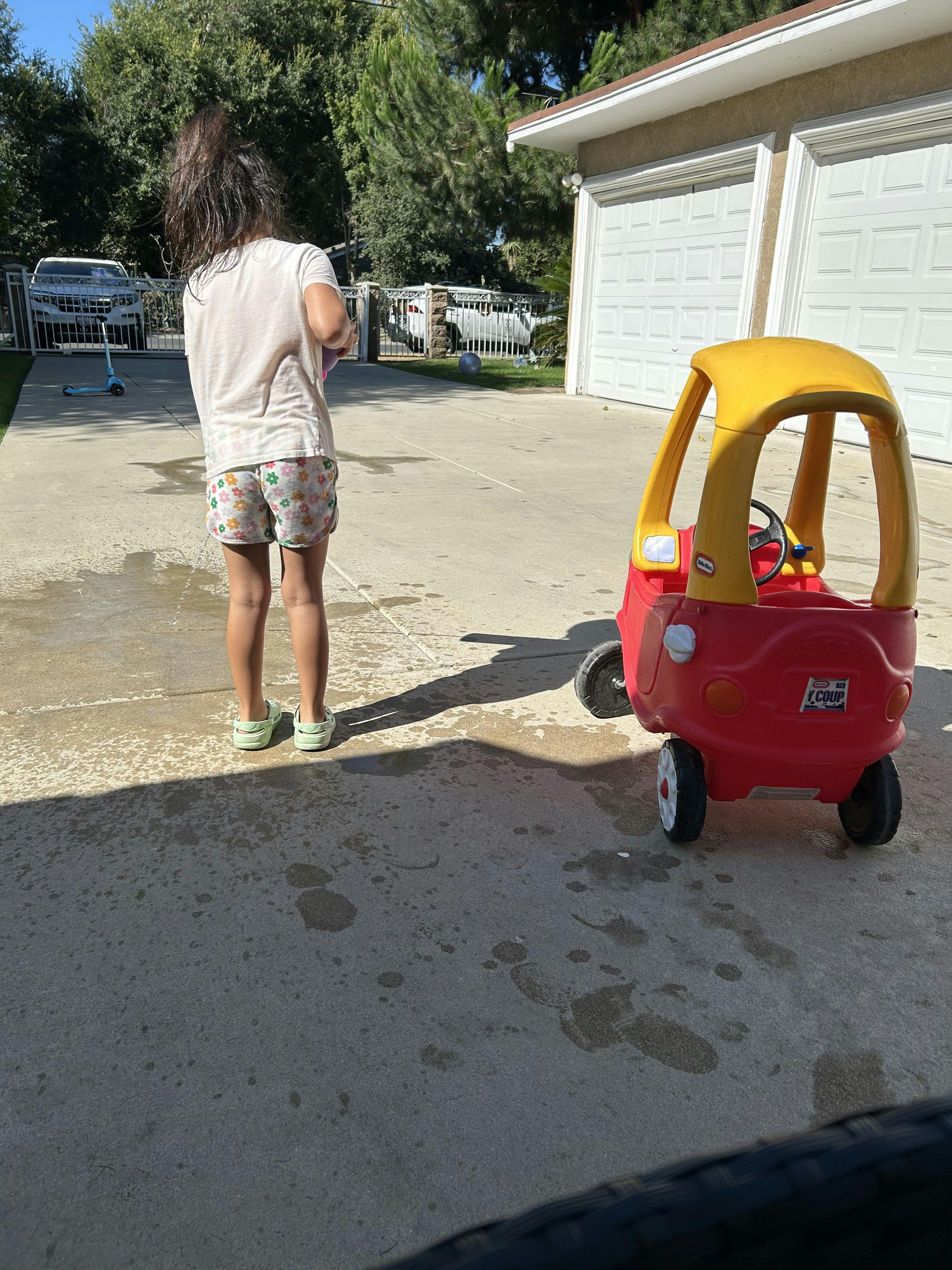 Child standing next to a toy car on a driveway