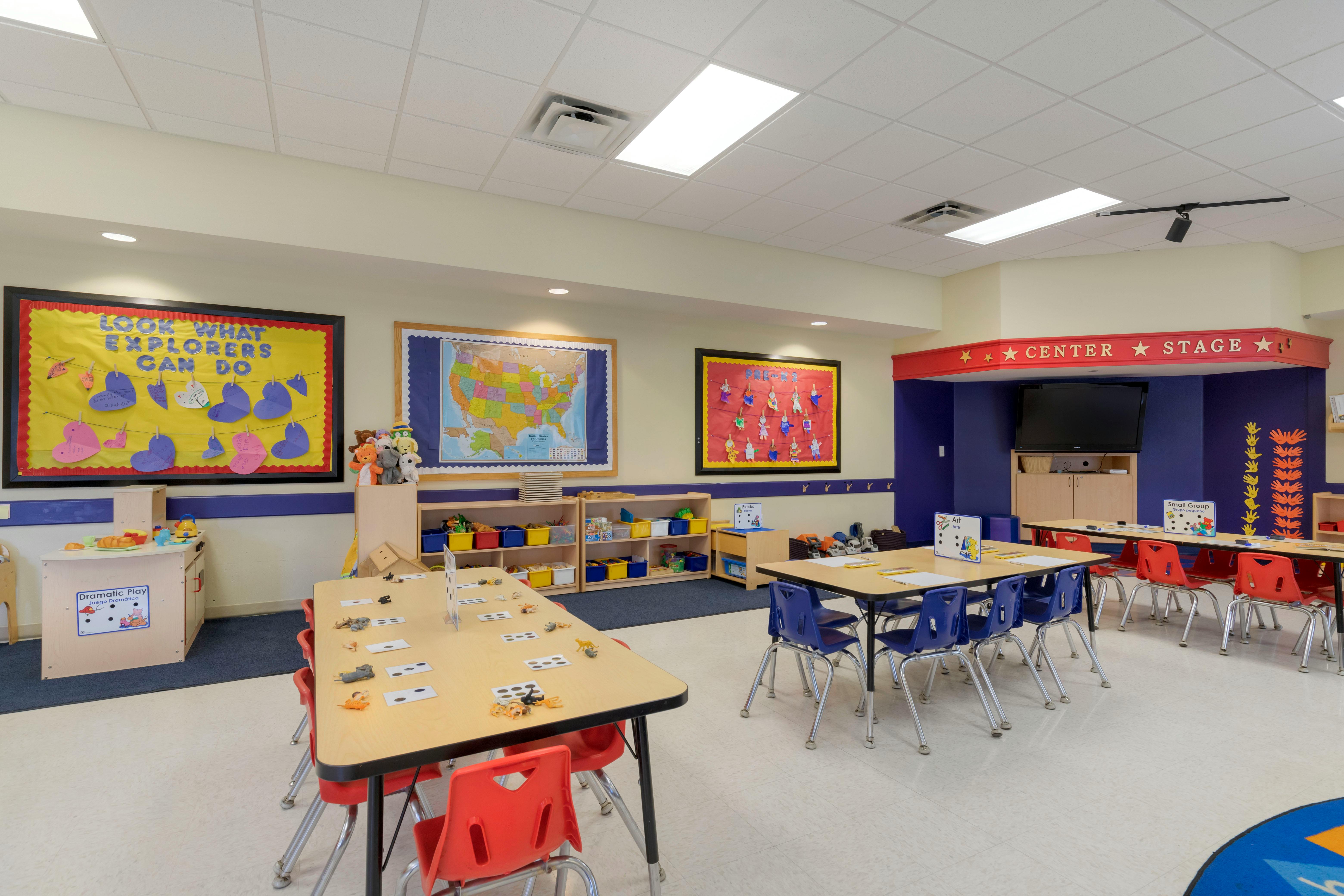 Empty classroom with small tables and chairs, bulletin boards, and learning stations