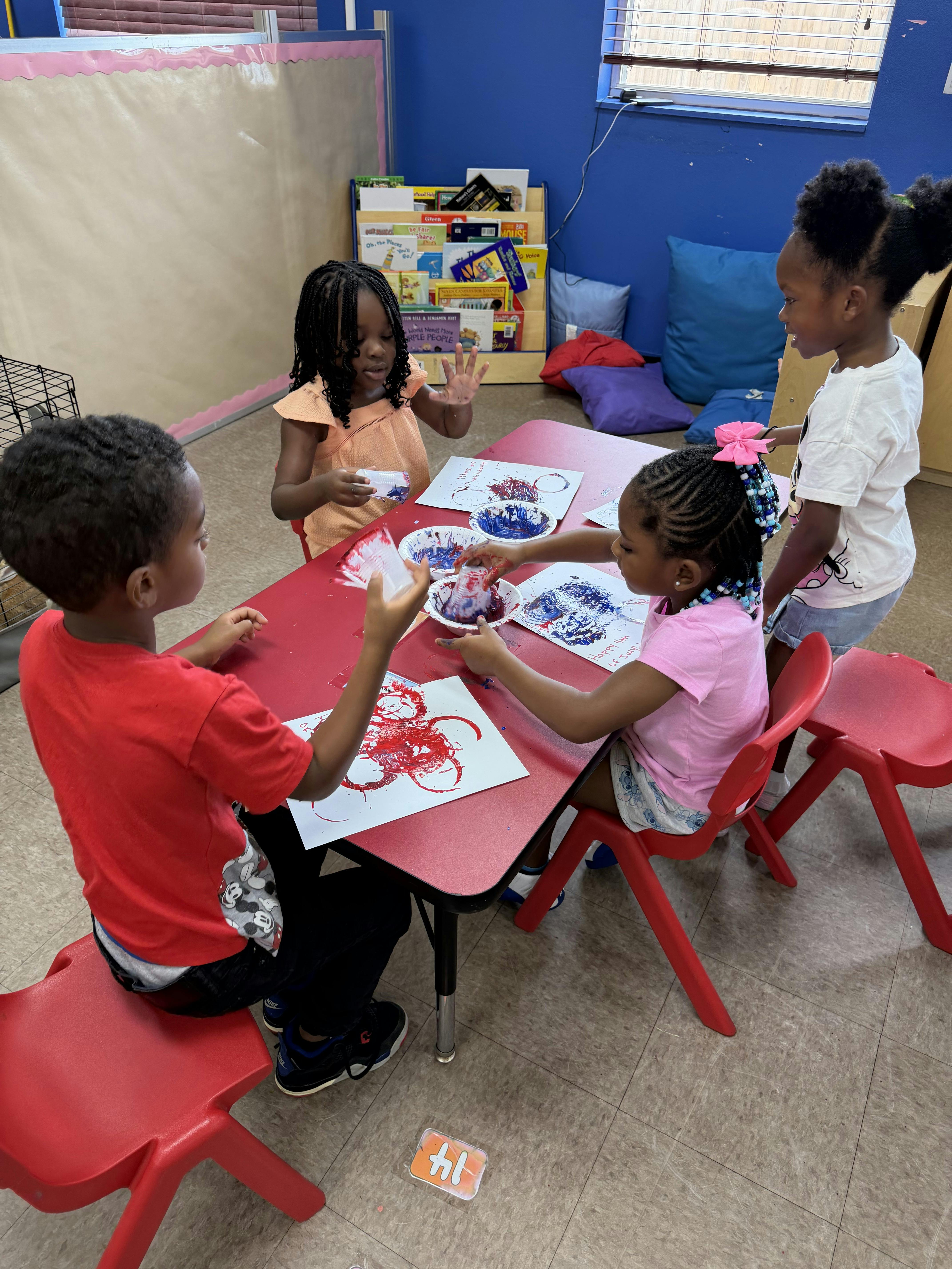 Children painting with small cups at a table in a classroom