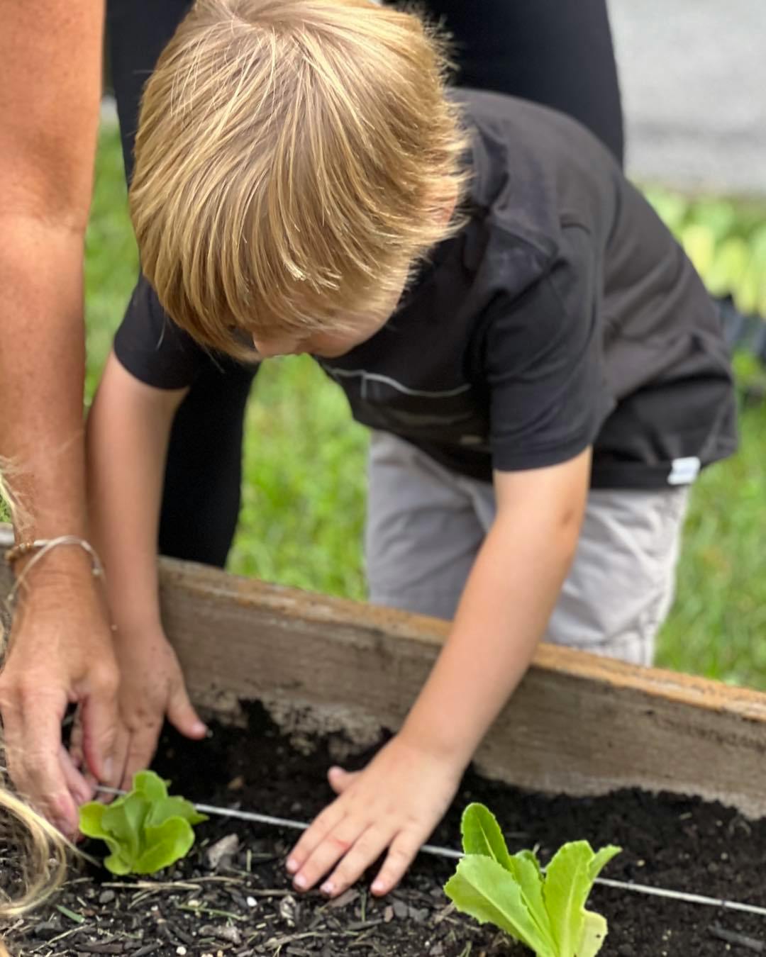 Child and person planting in a raised garden bed