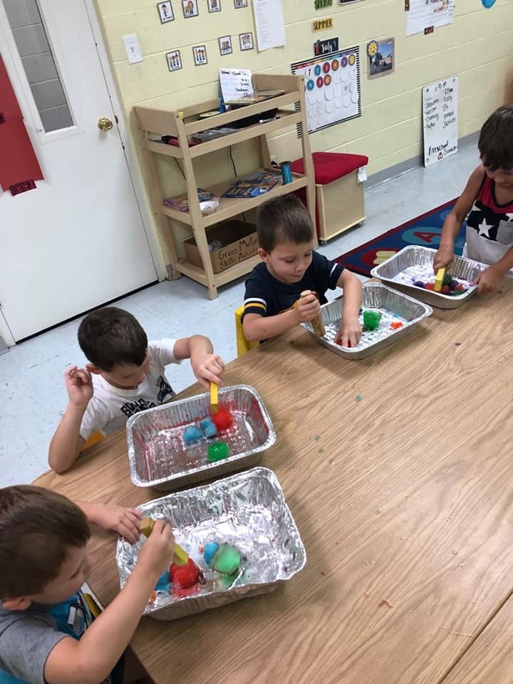 Children playing with colorful objects in foil trays at a table