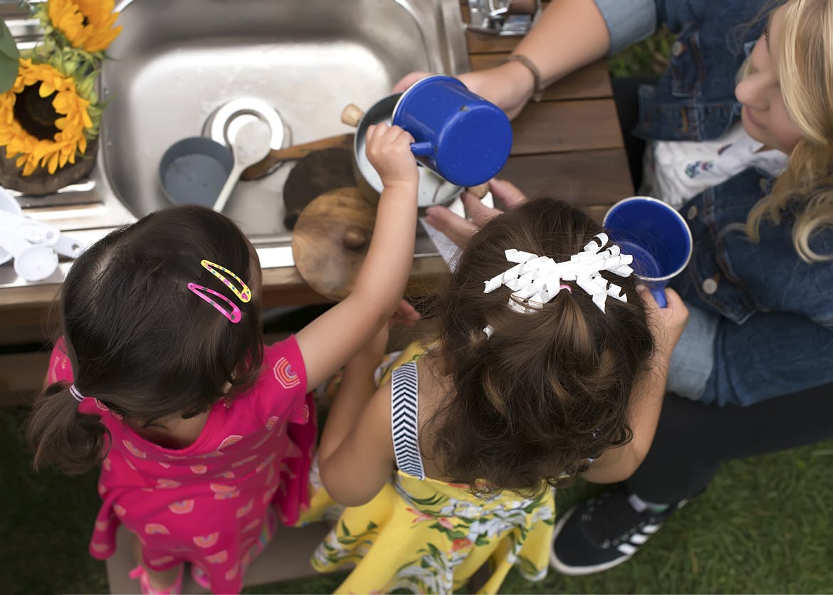 Two children playing with water and cups at a sink