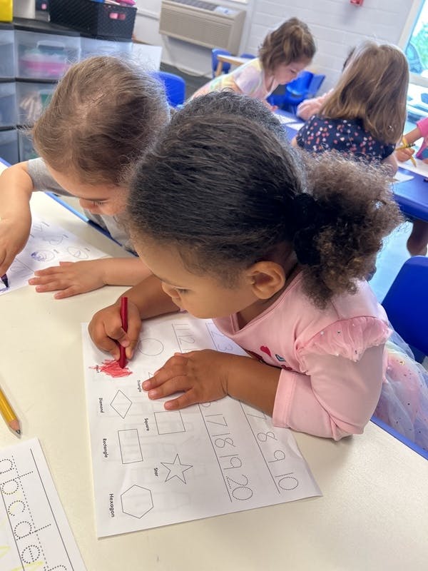 Child coloring a shape on a worksheet at a table