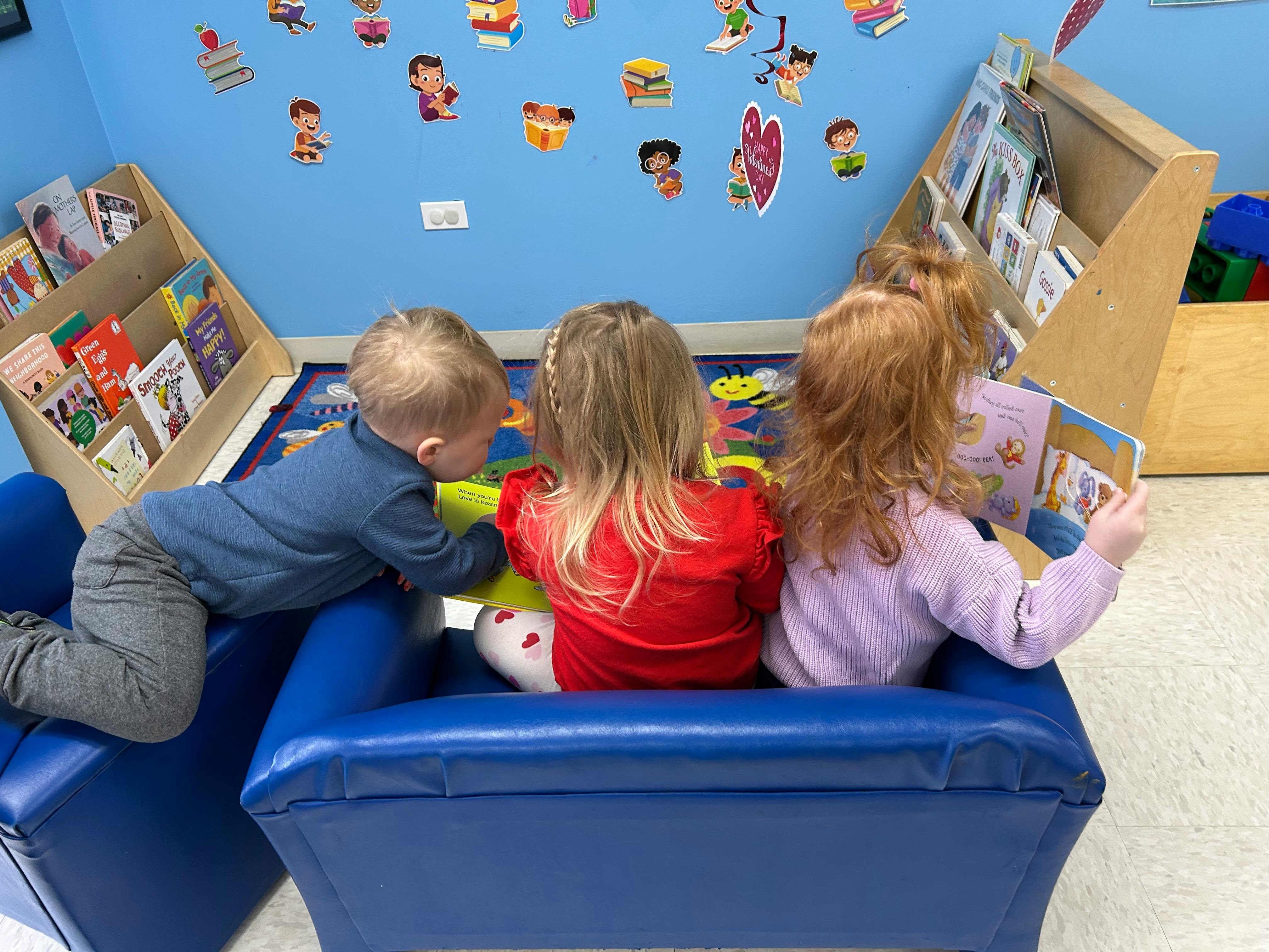 Three children playing in a blue soft play structure in a classroom