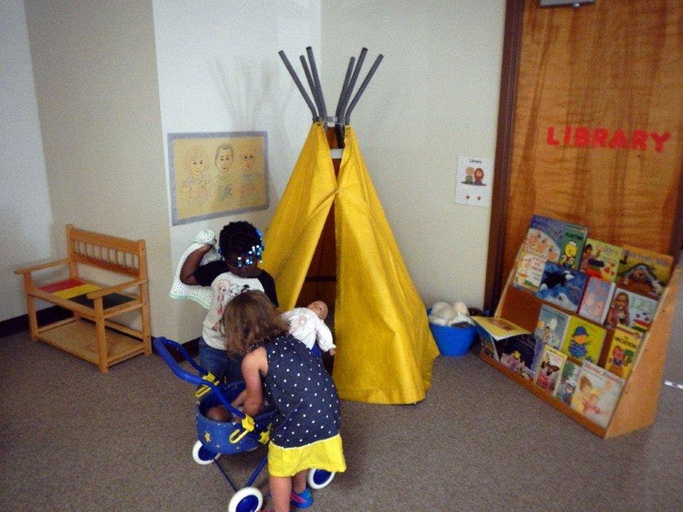 Two children playing with a toy stroller near a yellow tent in a library