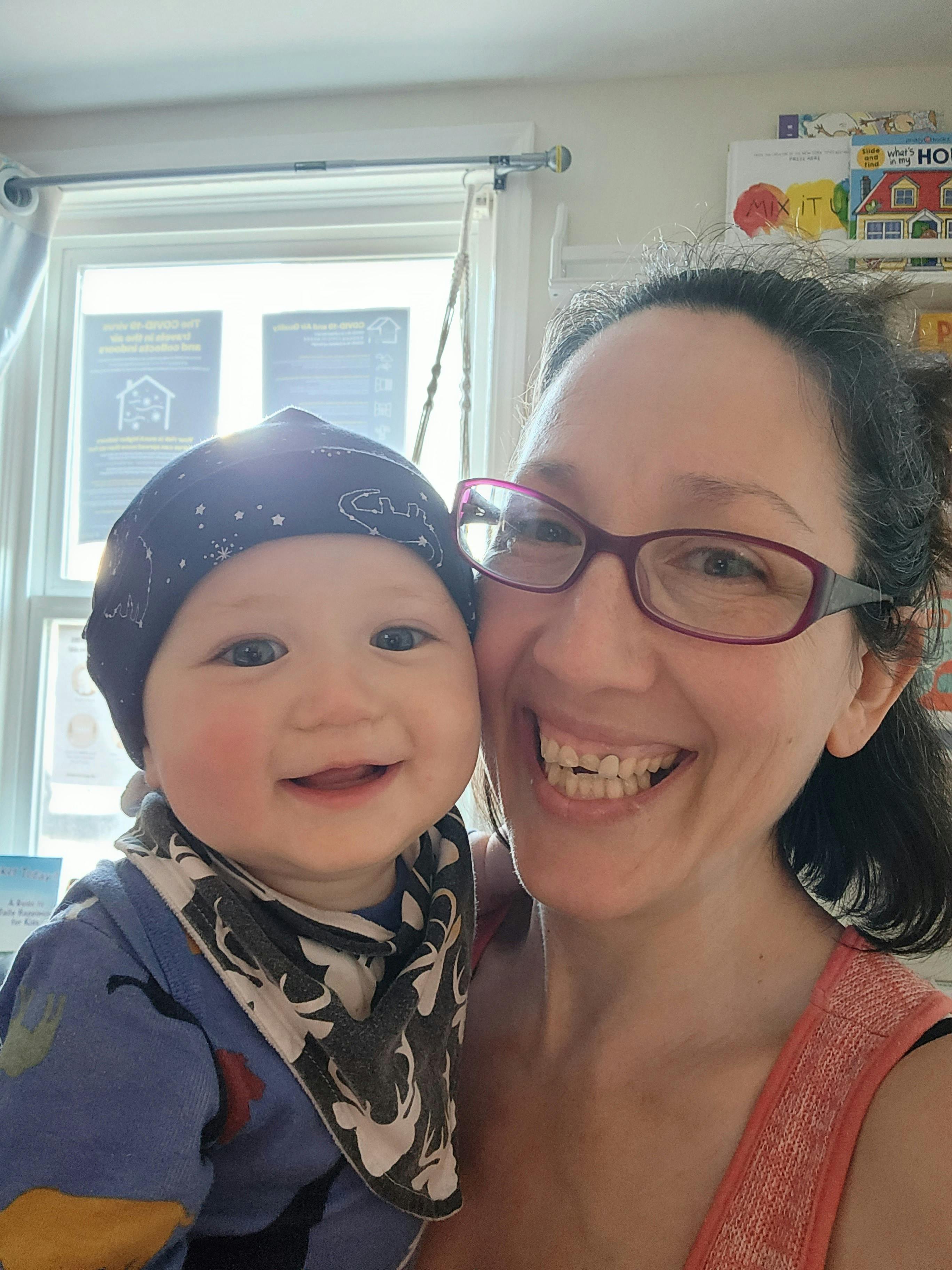 Person in glasses holding a child in a hat and bib