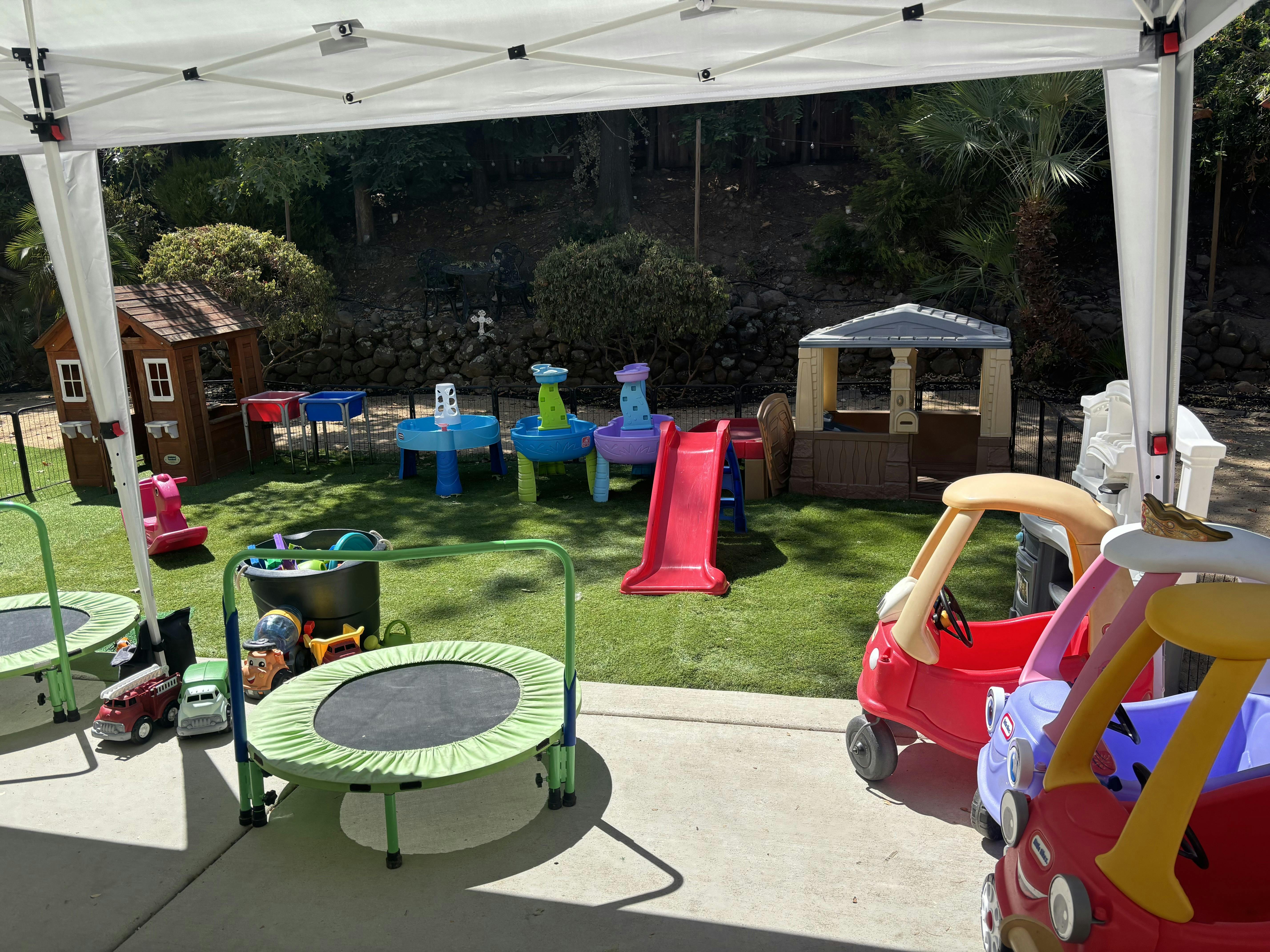 Outdoor play area with trampolines, toy cars, slide, and playhouses