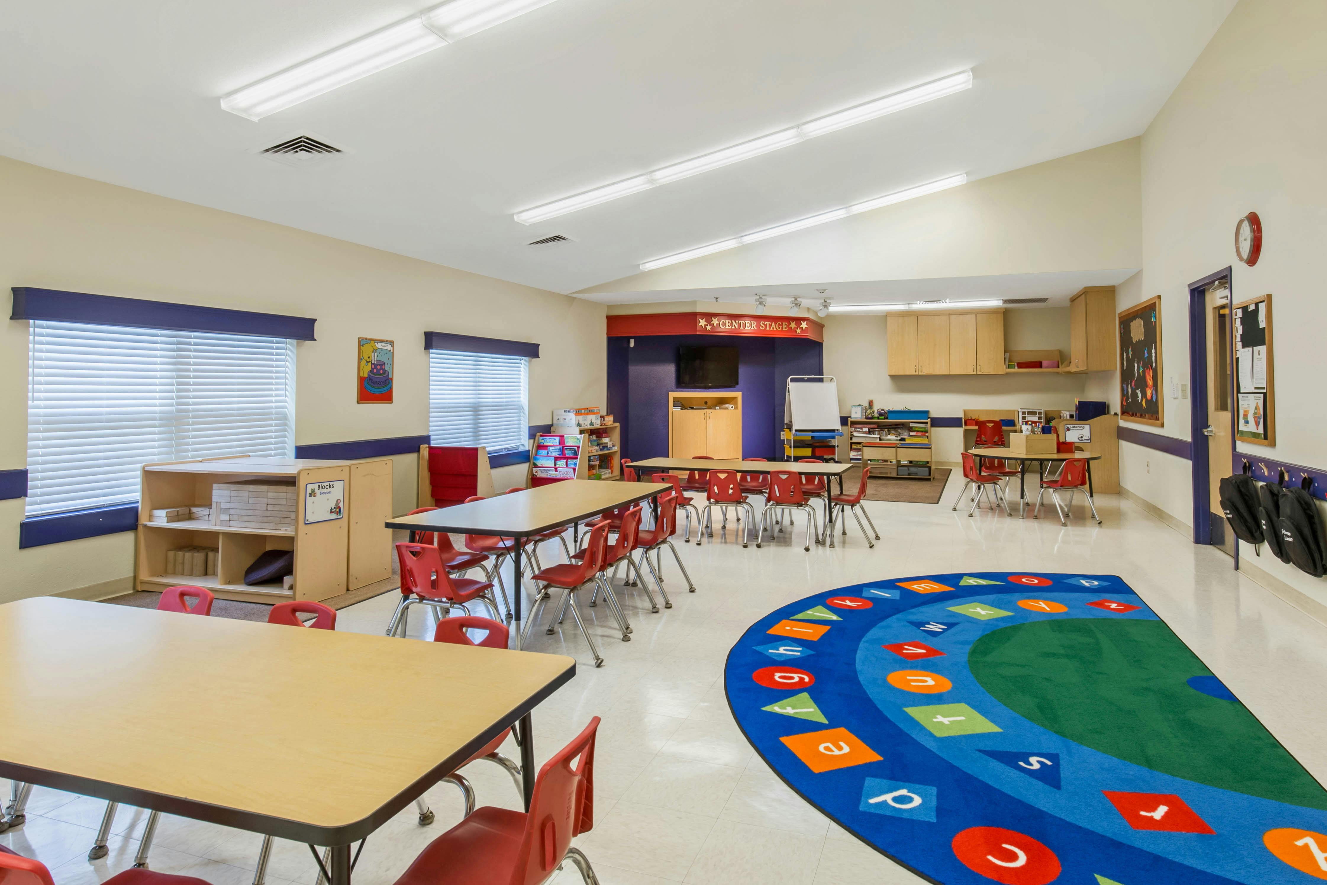 Classroom with tables, red chairs, storage, and an alphabet rug