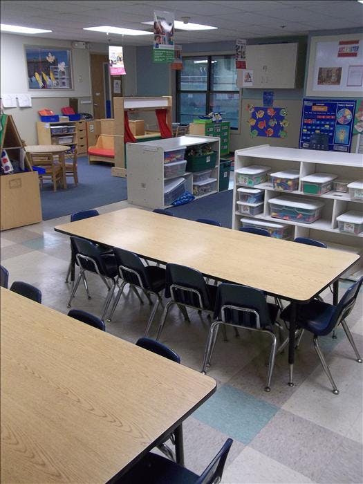 Classroom with tables and chairs, shelves with bins, and various learning materials