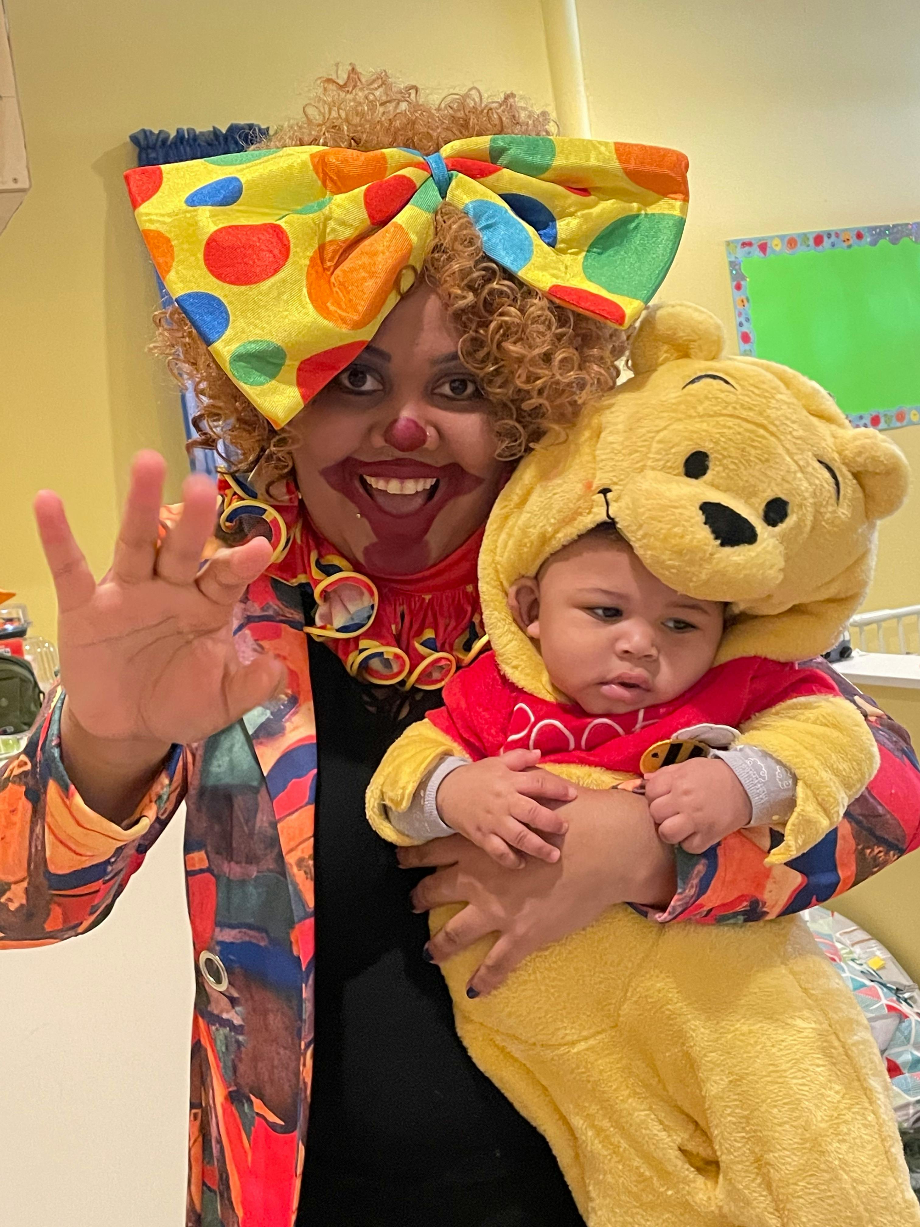 Person in clown makeup holding a child in a bear costume
