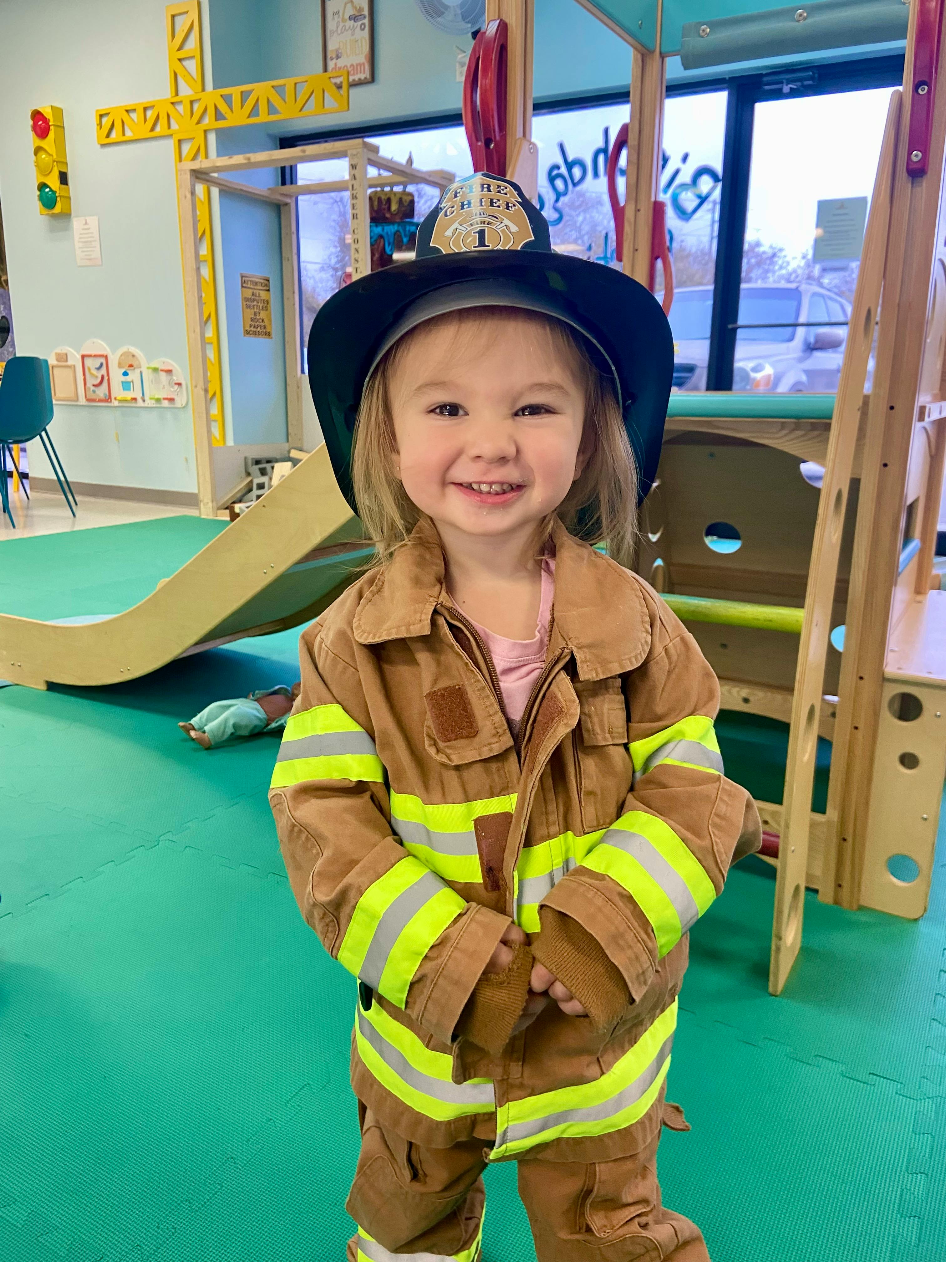 Child dressed in a firefighter costume and hat in a play area
