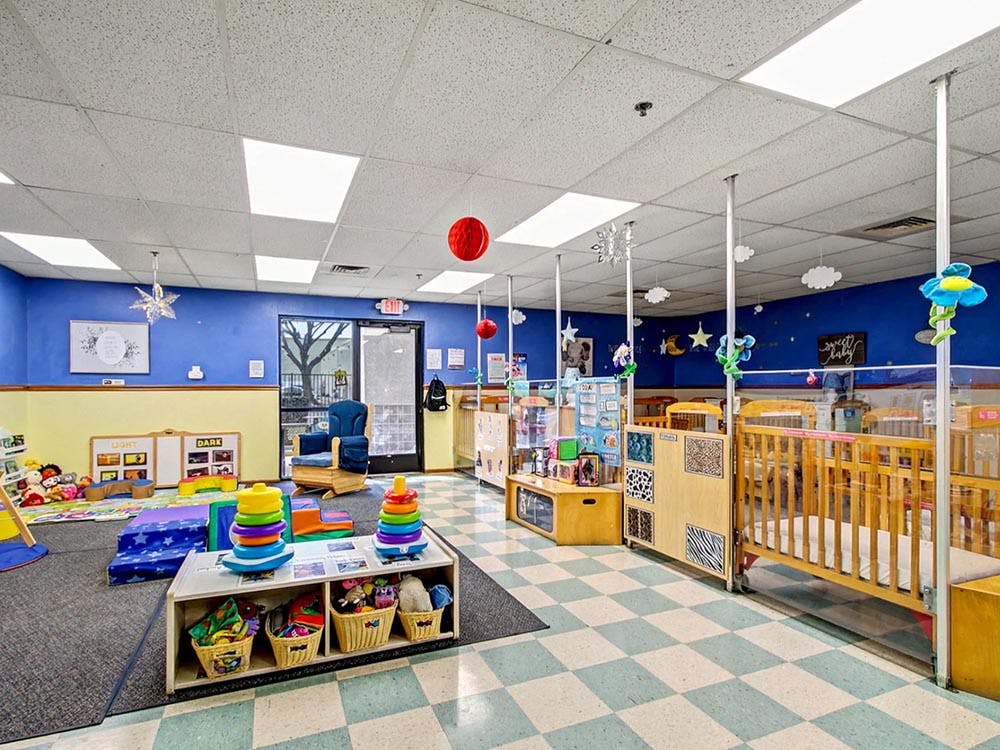 daycare room with cribs, play mats, shelves of toys, and a rocking chair