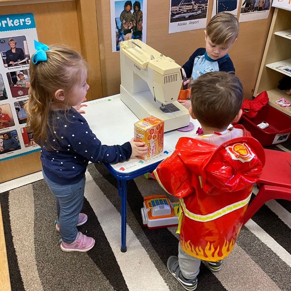 Three children playing with a sewing machine on a table