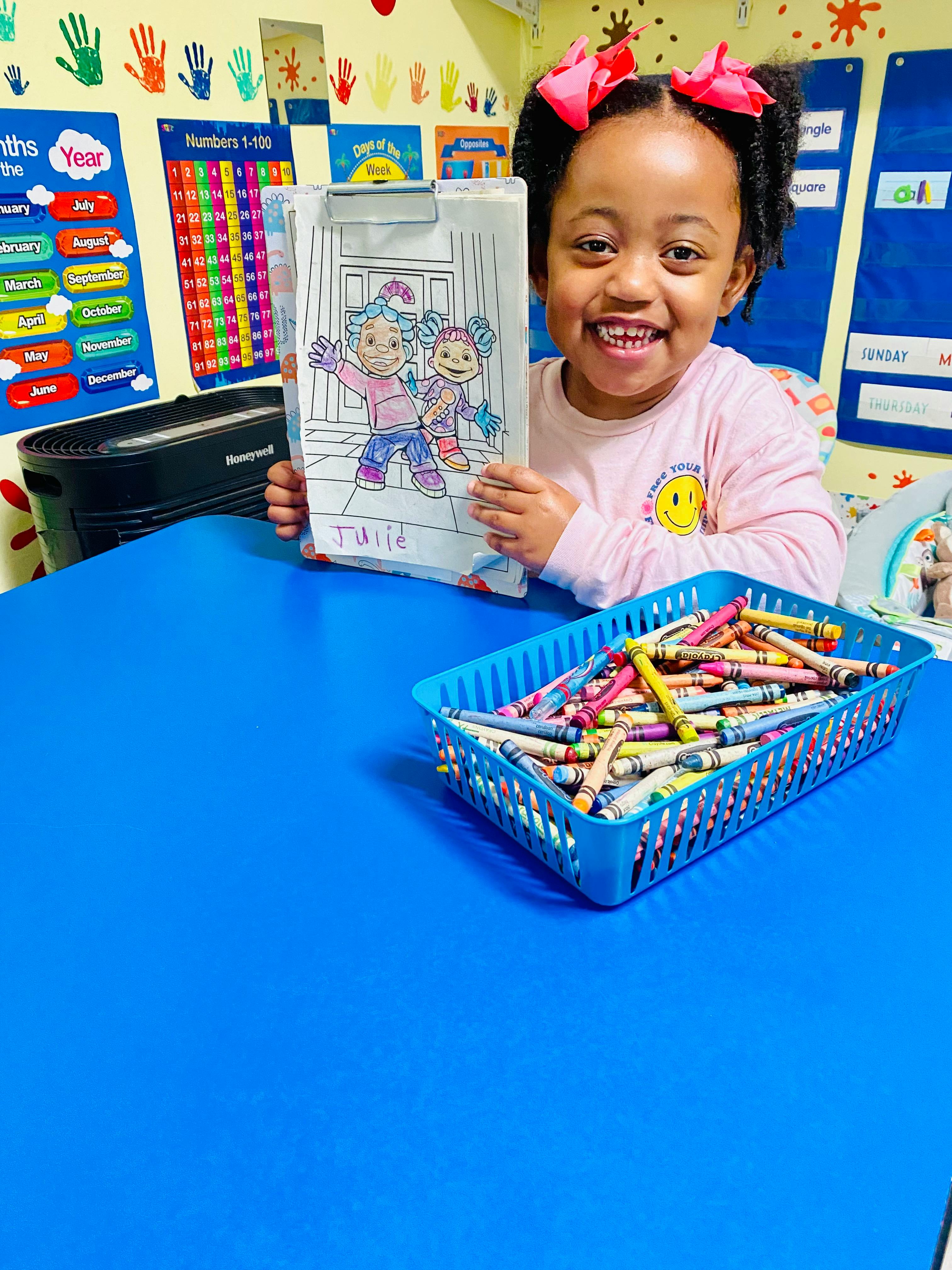 Child holding up a completed coloring page at a classroom table